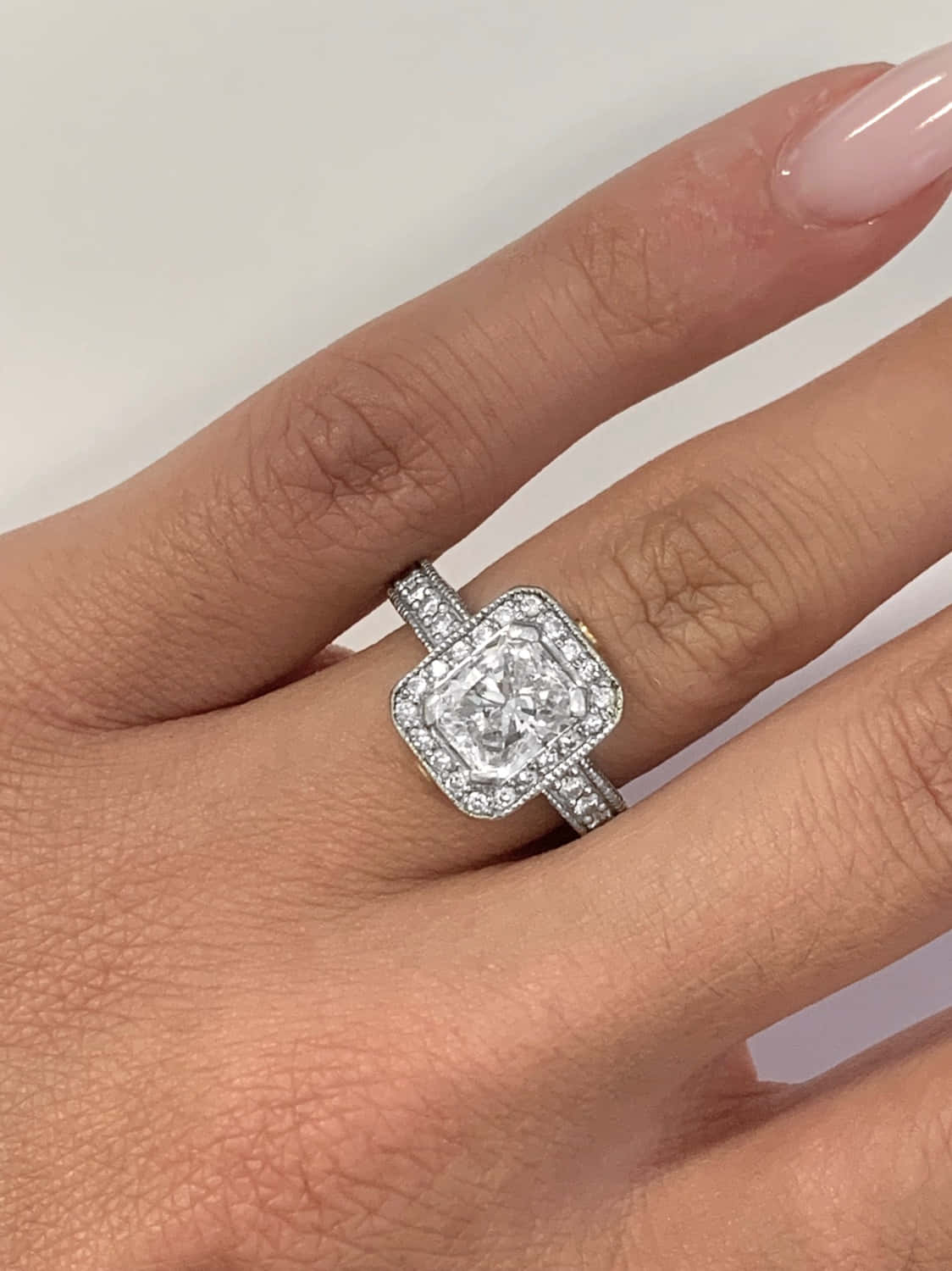 rings 桌布 壁紙 — 一隻帶有淡粉紅色指甲的手戴著閃爍的方形切割鑽石訂婚戒指，採用光環和密鑲鑲嵌。