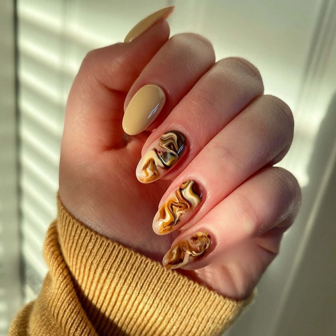Nail 桌布 壁紙 — 一隻帶有米色指甲的手，上面有旋轉的棕色、金色和黑色大理石圖案，靠在透過百葉窗過濾的柔和陽光下。