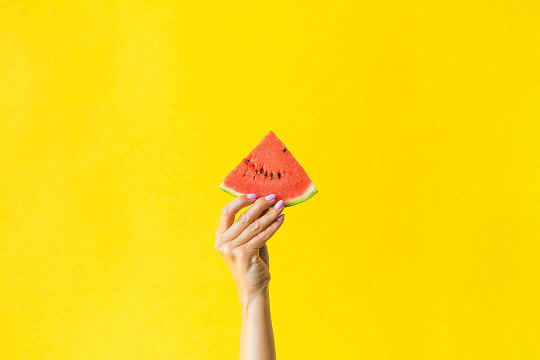 Watermelon 桌布 壁紙 — 一隻帶有粉紅色指甲的手在明亮的黃色背景前拿著一塊多汁的西瓜片。