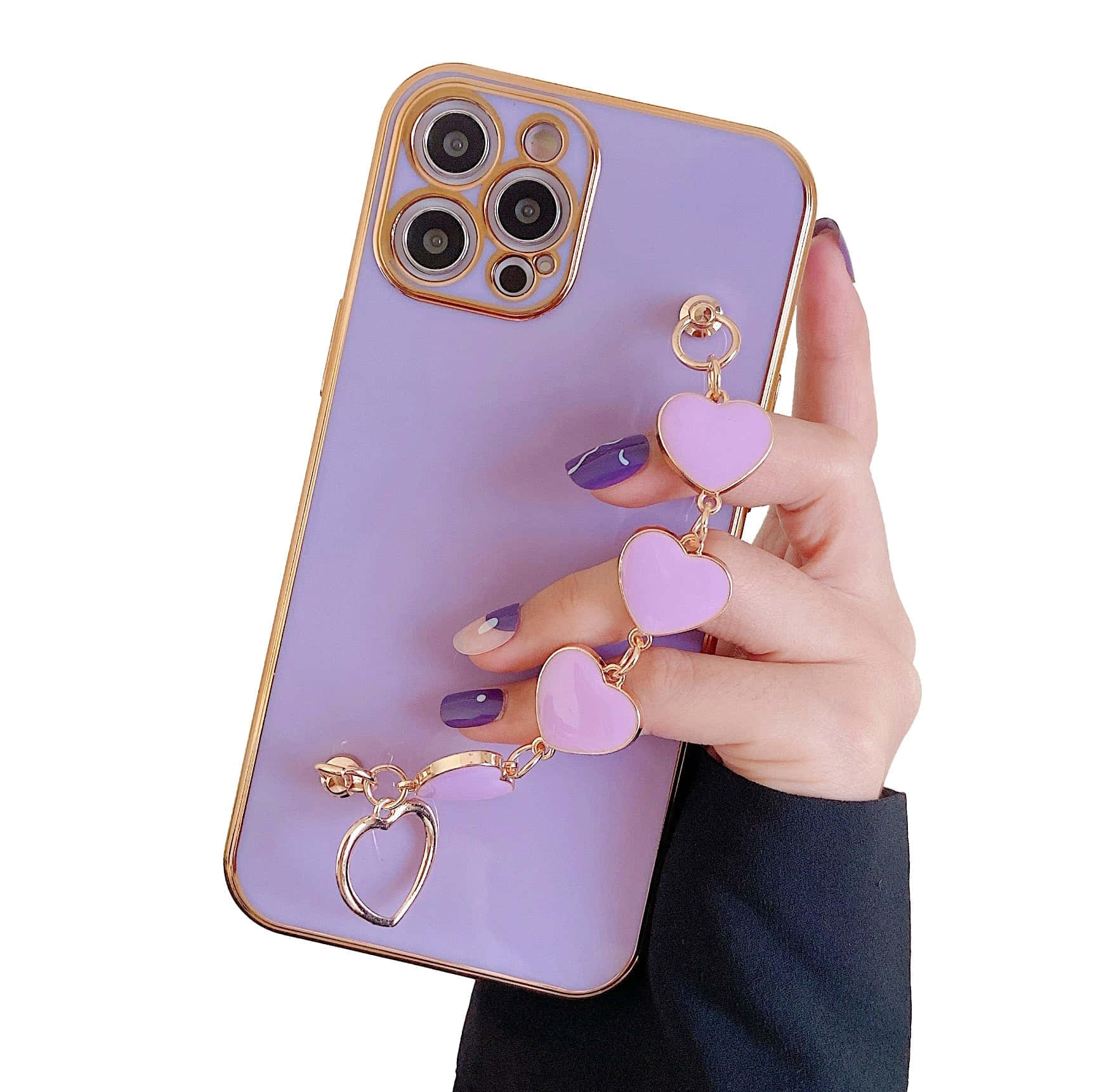 可愛 iPhone 桌布 桌布 壁紙 — 一隻帶有紫色指甲的手拿著一個帶有金色邊框和懸掛粉紅色心形吊飾的薰衣草色手機殼。