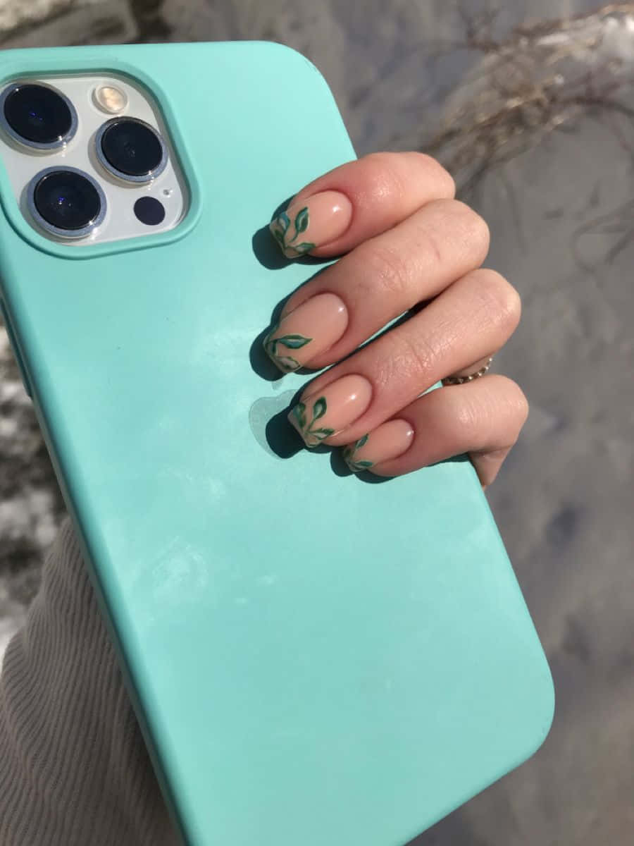 iPhone 12 桌布 壁紙 — 一隻帶有綠色葉子指甲藝術的手，在雪景戶外背景下拿著薄荷綠手機殼。