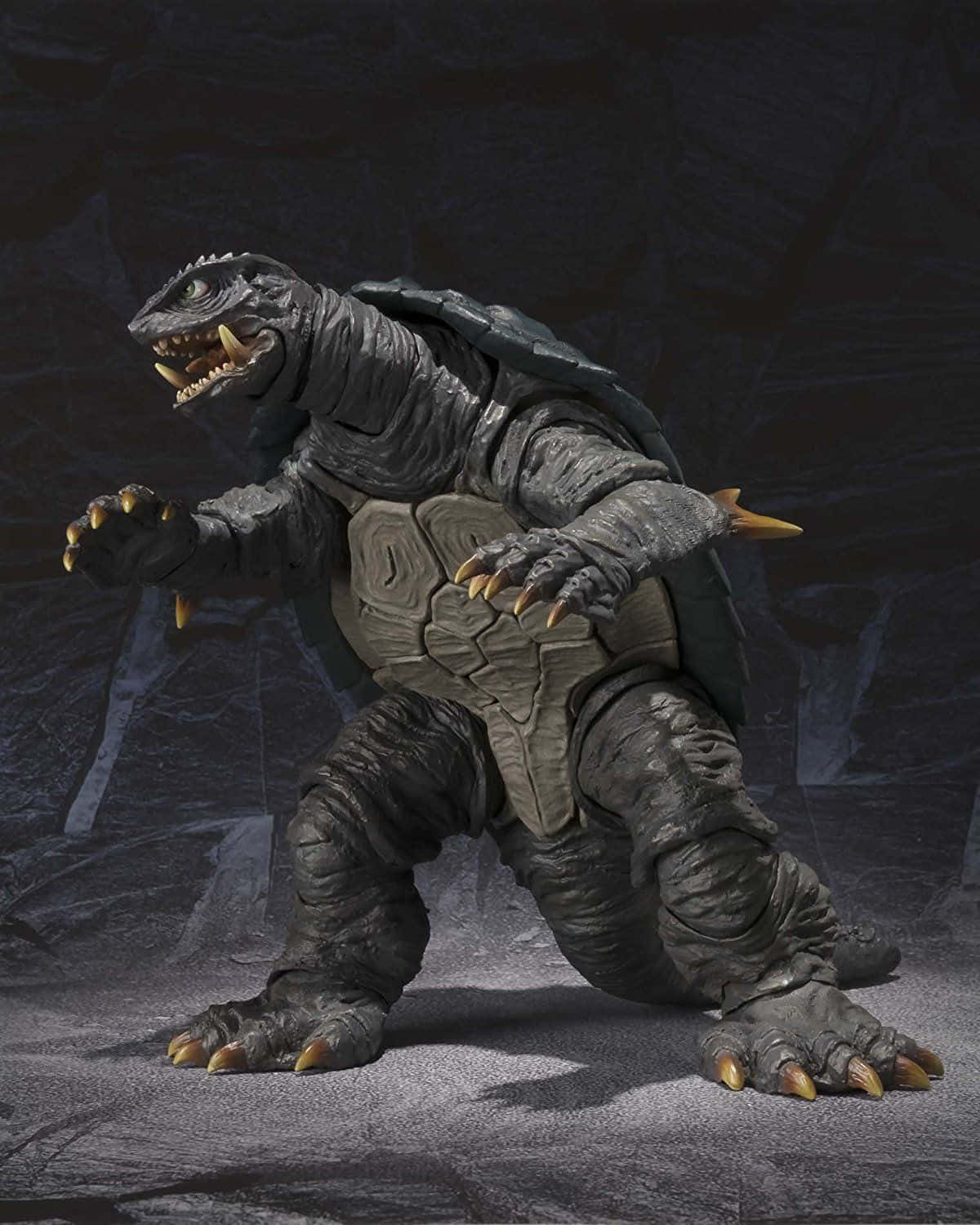 Gamera 桌布 壁紙 — 一隻帶有鋒利黃色爪子和尖刺殼的灰色哥吉拉般怪物，站在岩石洞穴中。