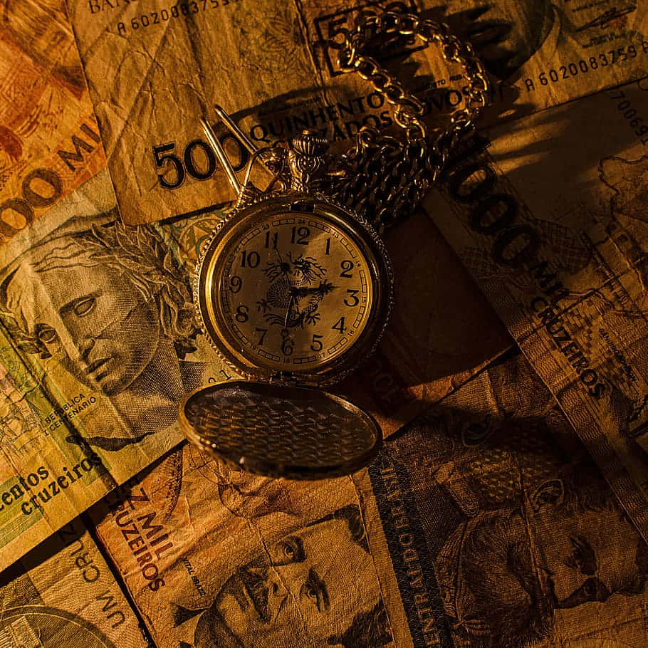 Money 桌布 壁紙 — 一隻帶有龍形設計的復古懷錶，放置在散落的巴西克魯塞羅紙幣上，沐浴在溫暖的金色光線中。