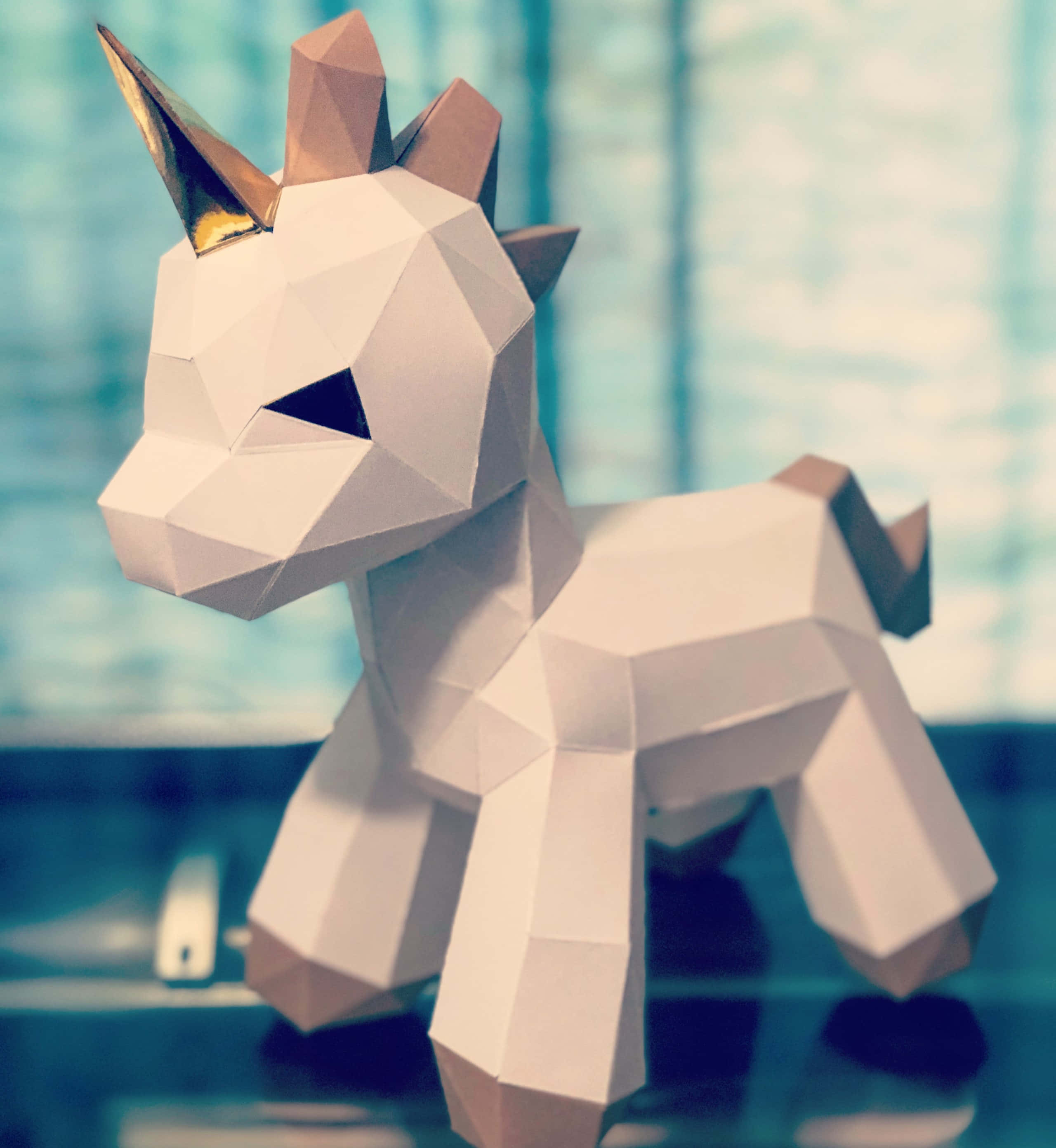 3d Unicorn 桌布 壁紙 — 一隻幾何紙製獨角獸，金色角，站在反射表面上，背景是模糊的藍色。