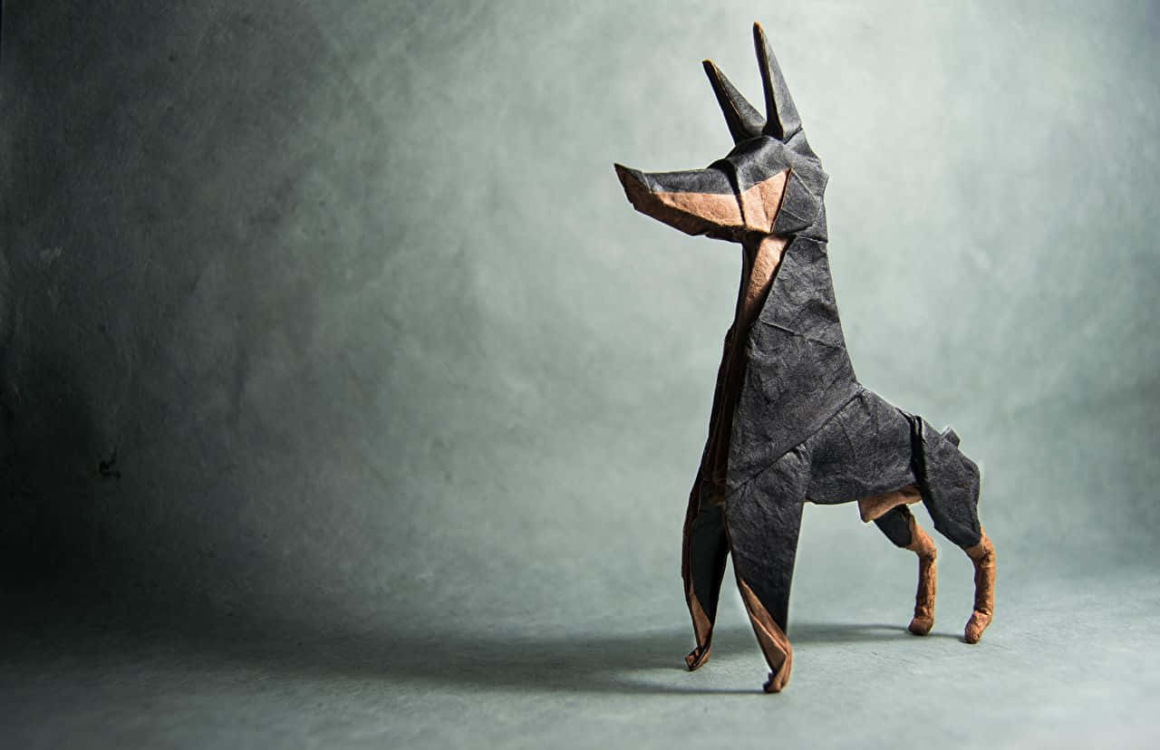 Doberman 桌布 壁紙 — 一隻引人注目的摺紙杜賓犬雕塑，在柔和灰色工作室背景和戲劇性燈光下蓄勢待發。