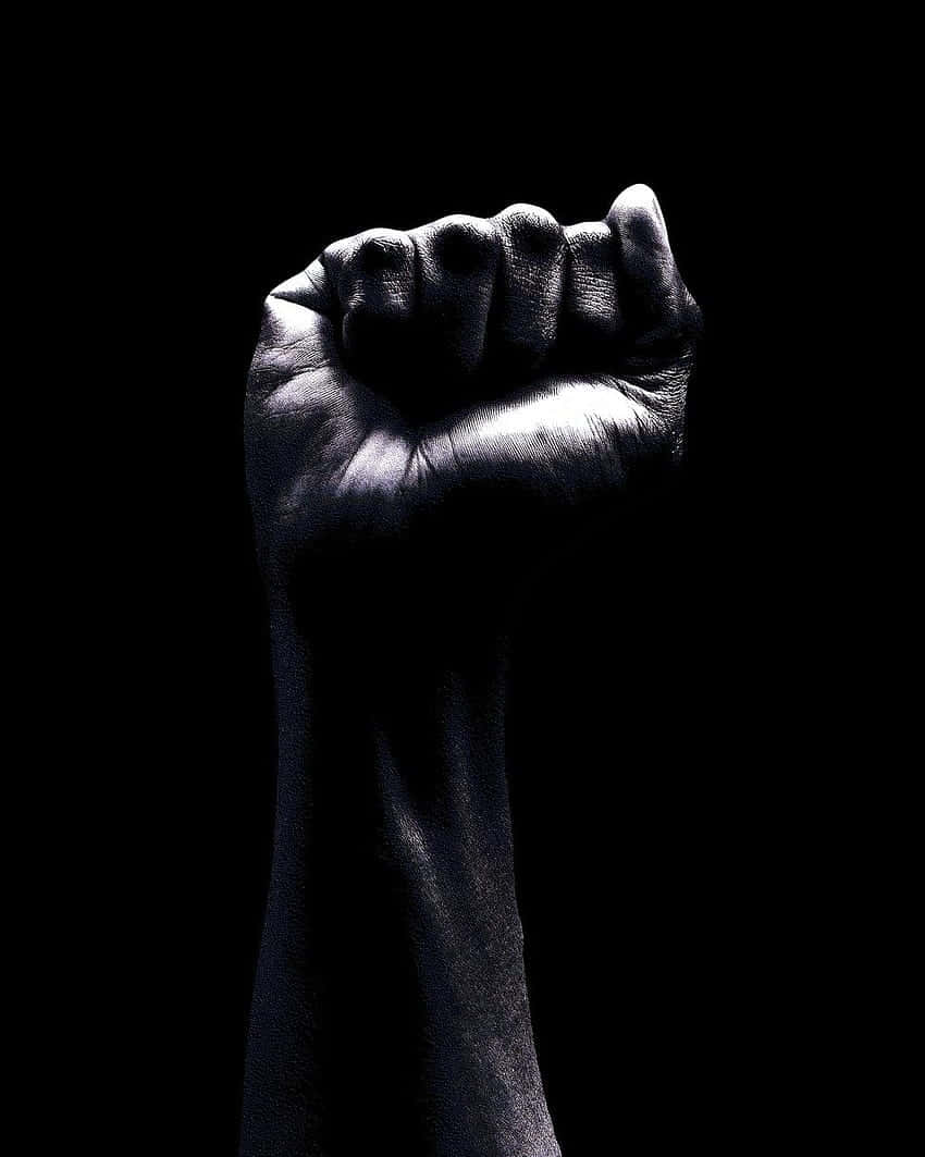 strength 桌布 壁紙 — 一隻強而有力的拳頭在純黑背景上被照亮，象徵抵抗與團結。