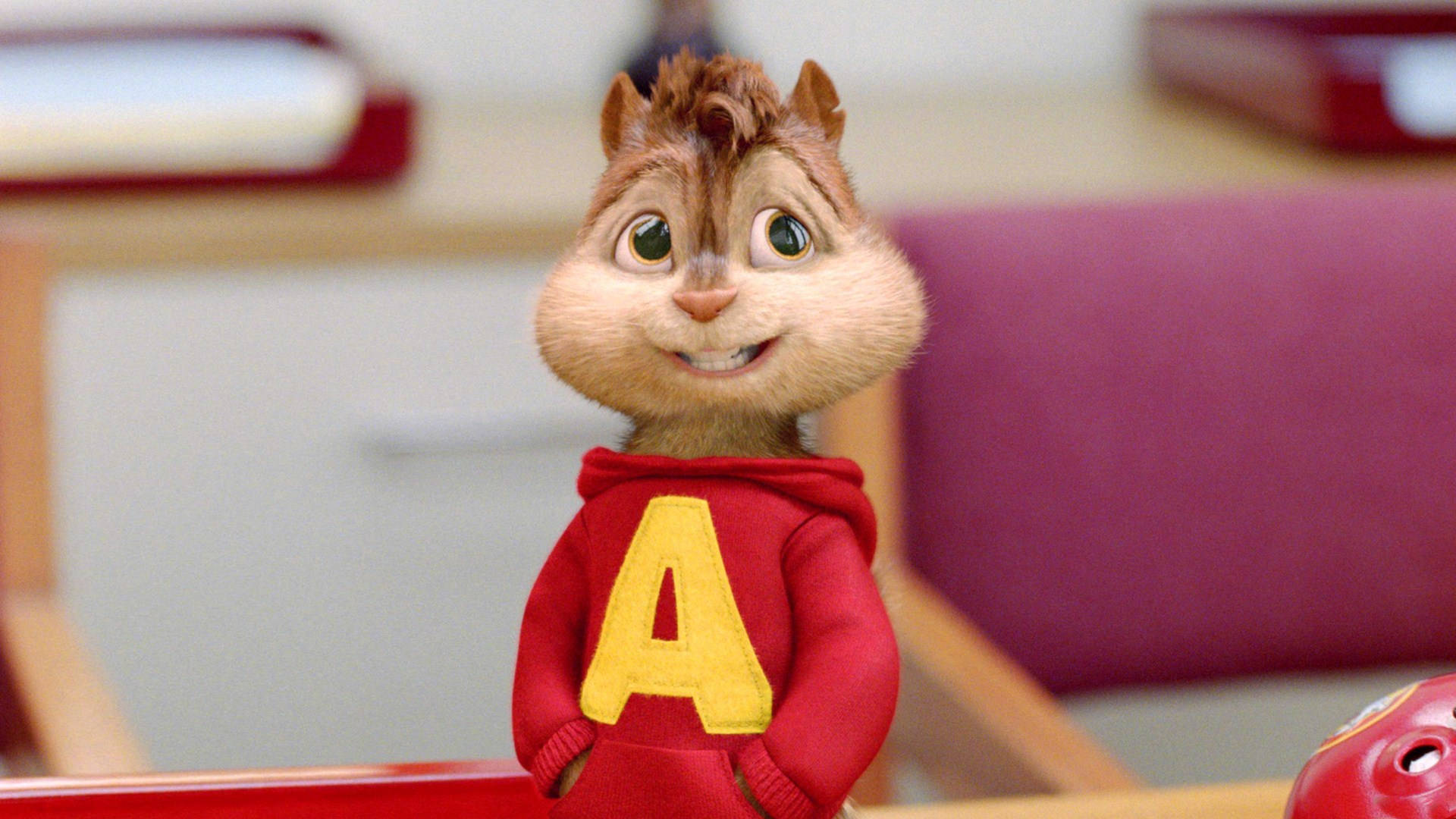 Chipmunks 桌布 壁紙 — 一隻快樂的動畫花栗鼠穿著紅色連帽衫，上面有黃色的「A」，在教室環境中燦爛地微笑。