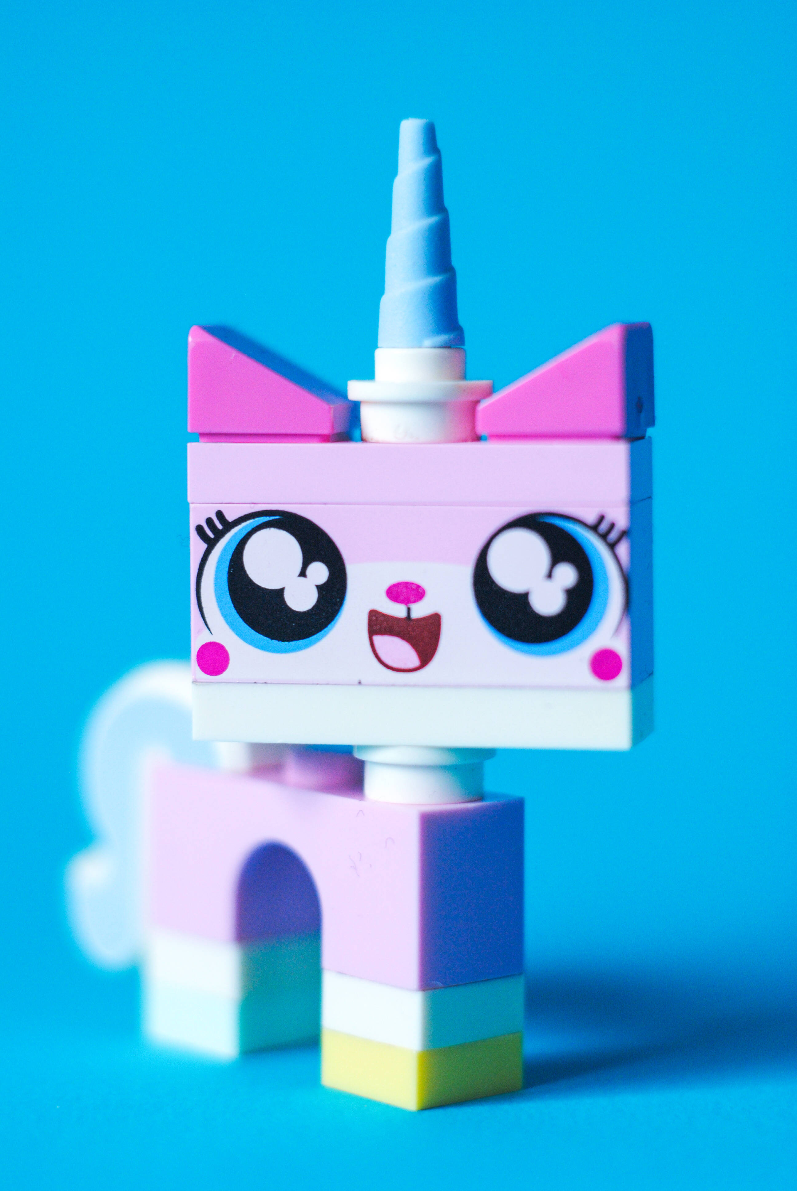 Happy Anniversary 桌布 壁紙 — 一隻快樂的粉紅色LEGO獨角獸，有大藍眼睛和螺旋角，站在鮮豔的藍色背景前。