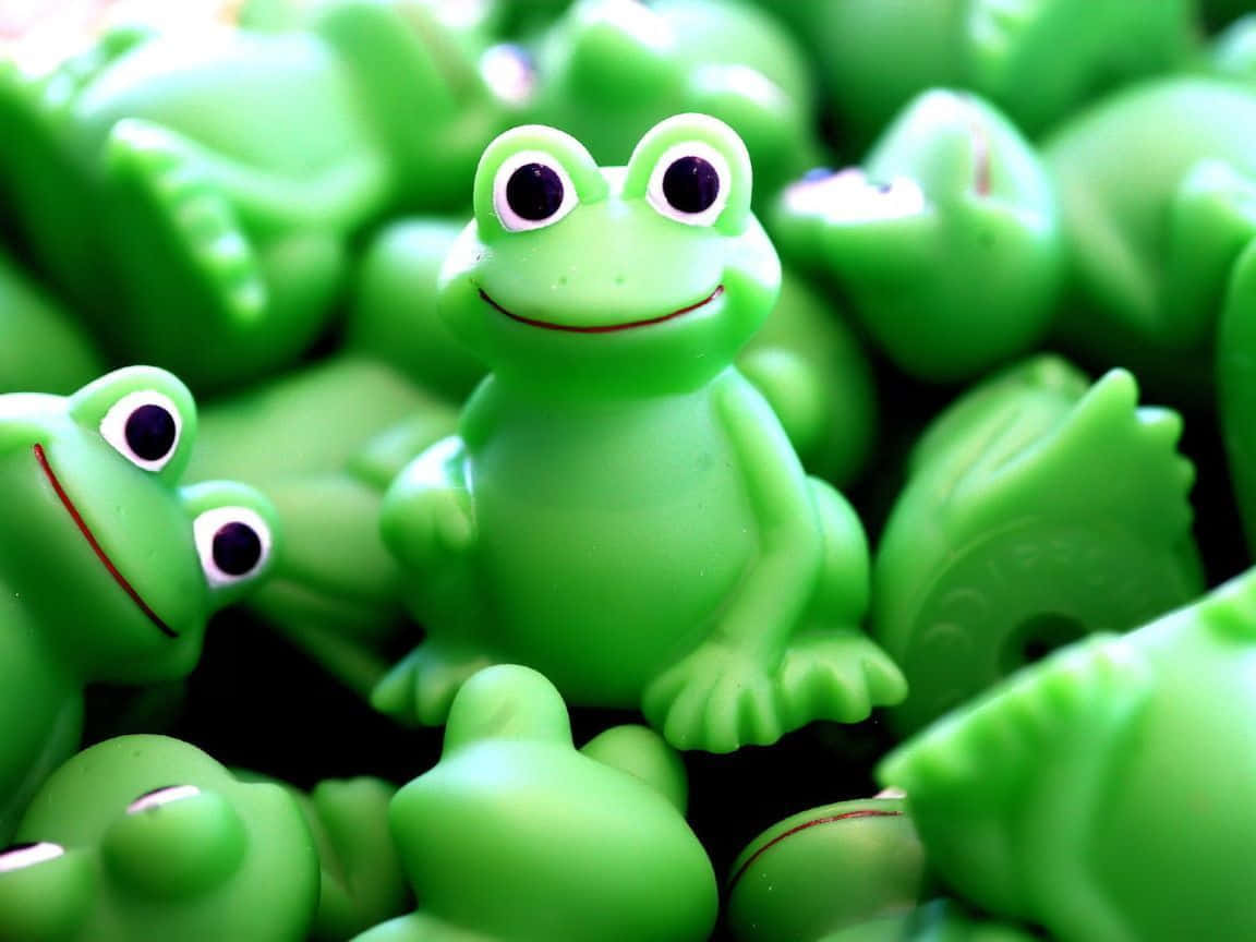 Frog 桌布 壁紙 — 一隻快樂的綠色塑膠青蛙玩具在柔焦中，在一堆相同的青蛙中燦爛地微笑。