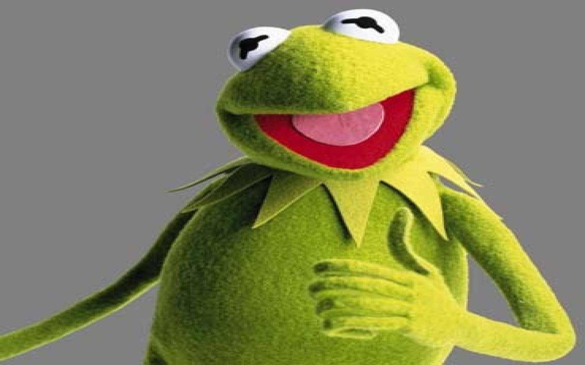 kermit 桌布 壁紙 — 一隻快樂的綠色青蛙玩偶，有著寬闊的紅嘴巴和白色的眼睛，在純灰色背景上豎起大拇指。