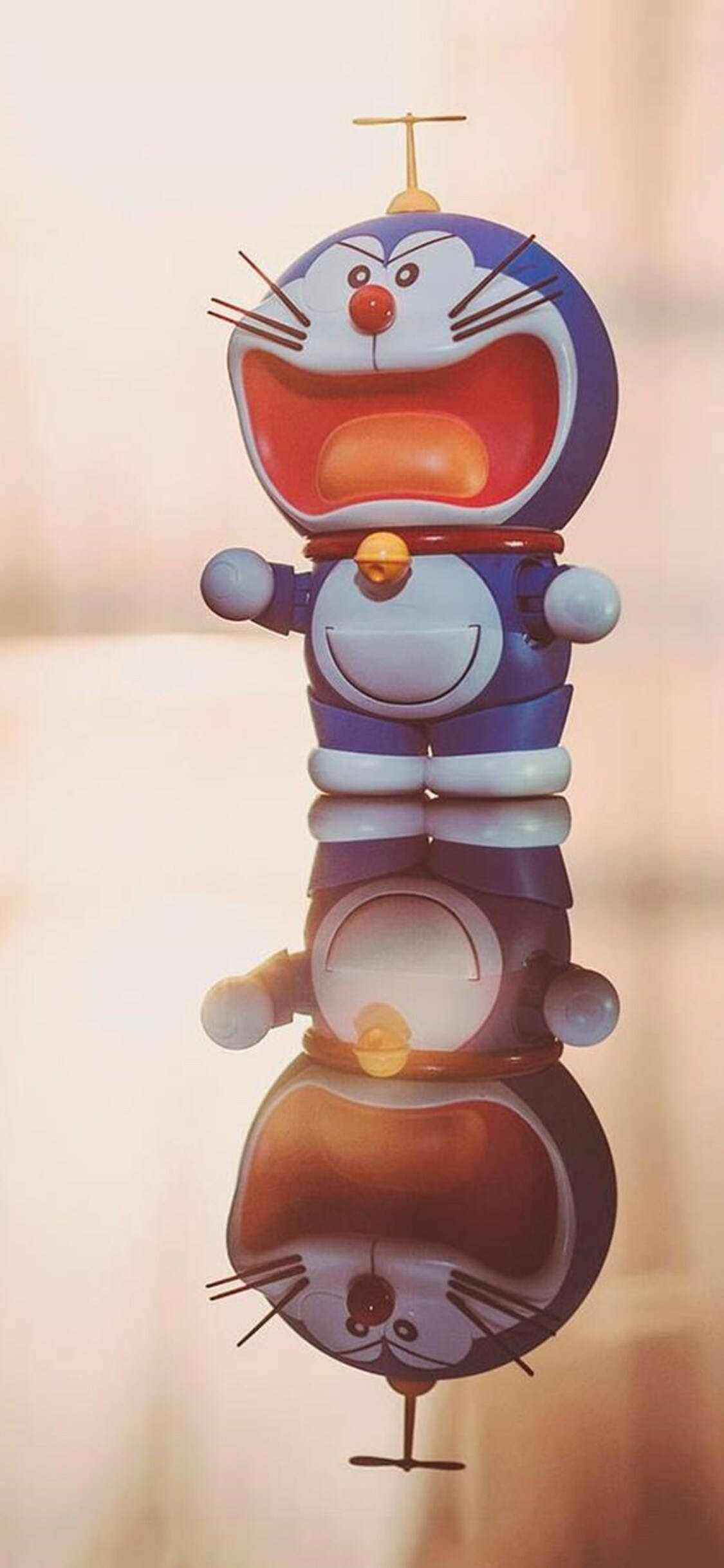 Doraemon 桌布 壁紙 — 一隻快樂的藍色機器貓，有紅色鼻子和天線，垂直堆疊，在光滑表面上倒映出上下顛倒的倒影。
