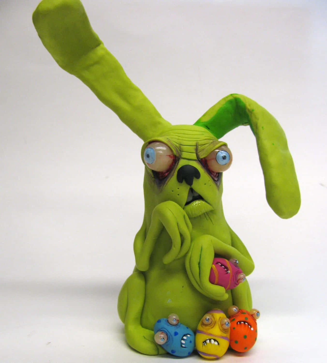 Creepy Easter Bunny 桌布 壁紙 — 一隻怪異的綠色黏土兔子，有著凸出的眼睛和細小的怪物同伴，坐在純白色背景前。