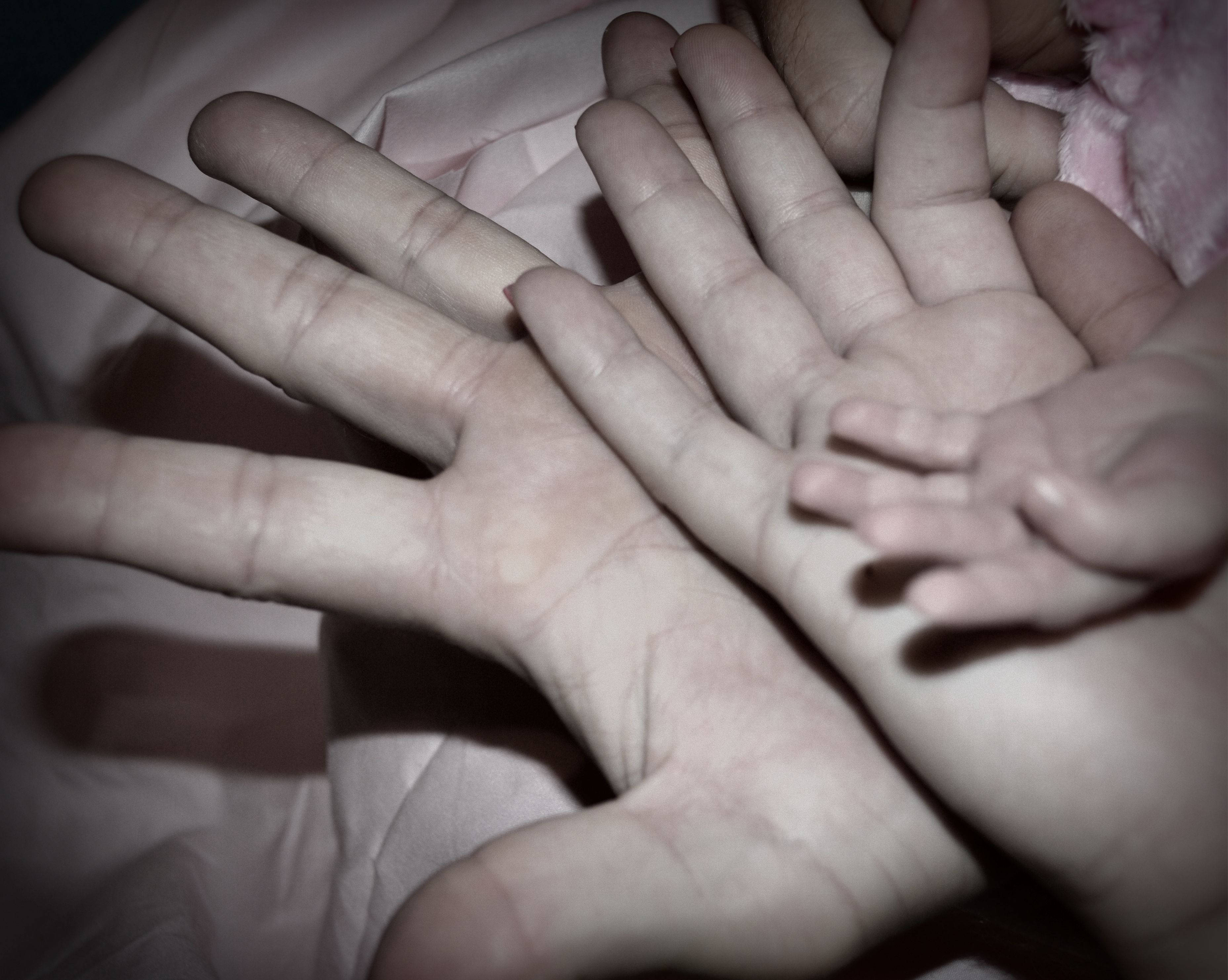 Mom 桌布 壁紙 — 一隻成年人的手溫柔地托著嬰兒的小手，放在柔軟的粉紅色布料上，呈現溫馨親密的時刻。