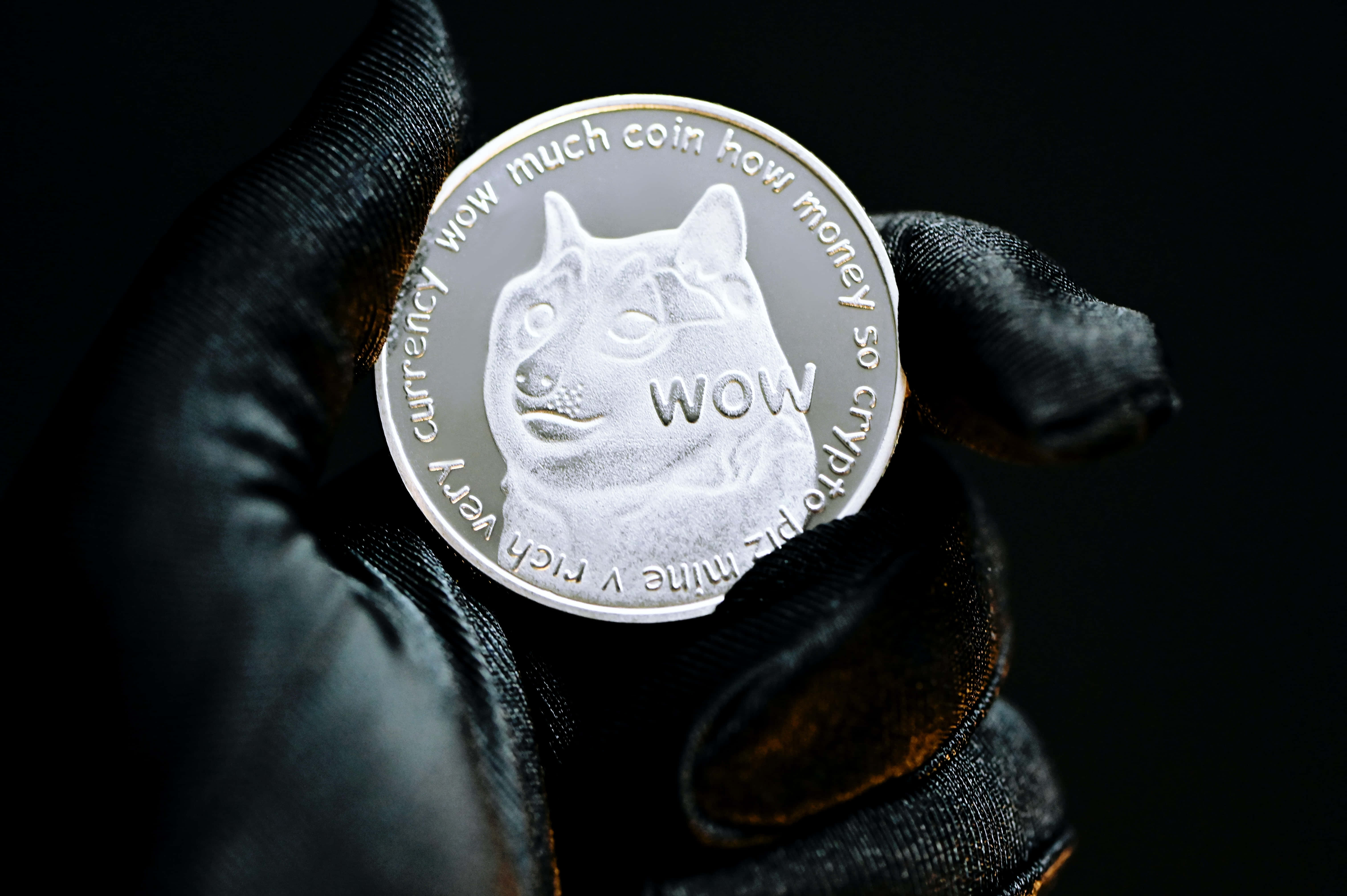 Dogecoin 桌布 壁紙 — 一隻戴手套的手在黑色背景上拿著一枚銀色狗狗幣，上面有柴犬和「WOW」及加密貨幣文字。