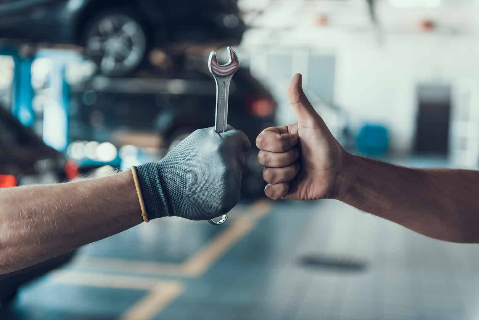 Mechanic 桌布 壁紙 — 一隻戴手套的手拿著扳手，而另一隻手在汽車維修廠豎起大拇指。