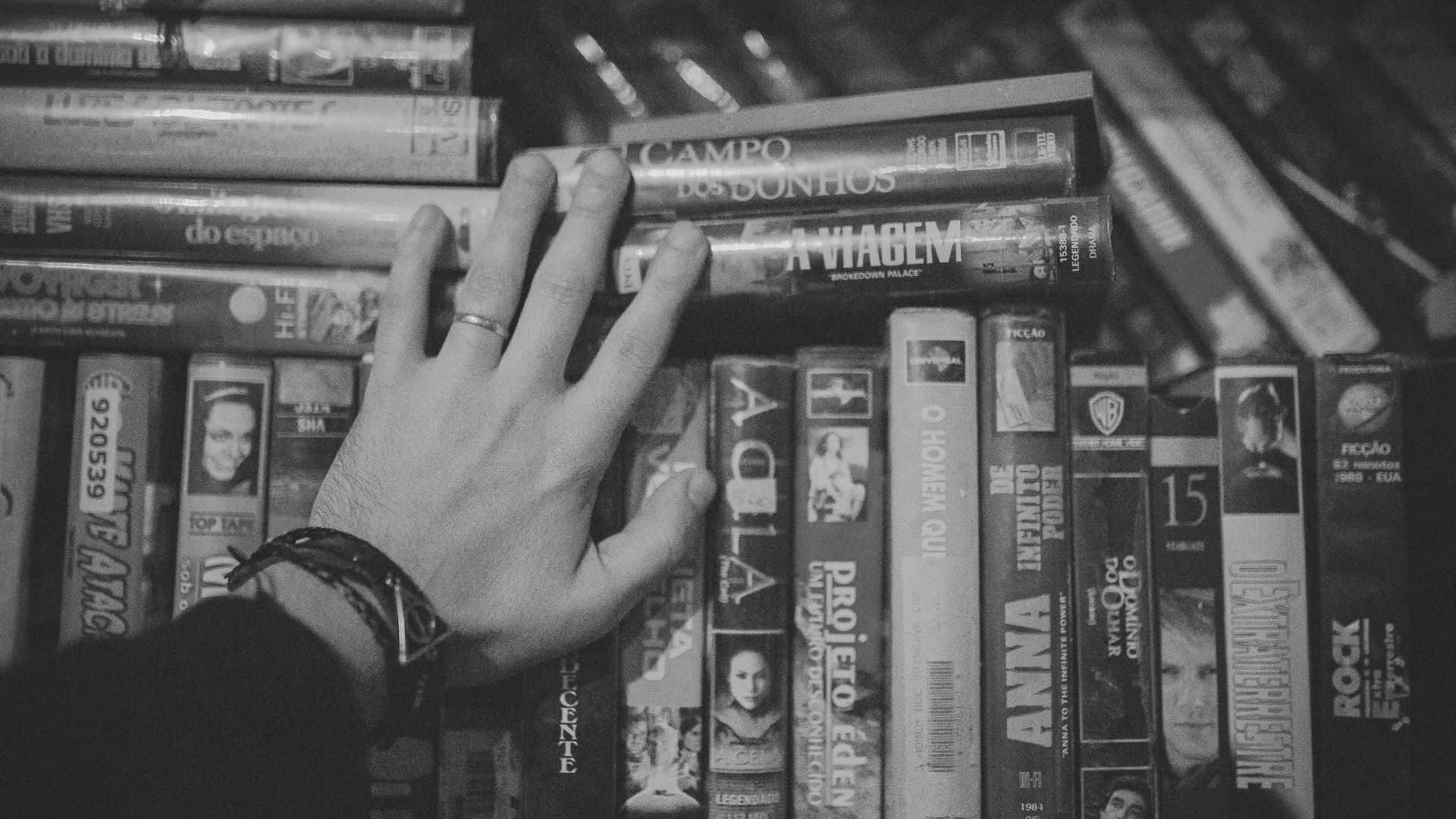 Black And White Movie 桌布 壁紙 — 一隻戴有戒指和手鐲的手輕輕放在一堆復古VHS錄影帶上，以單色拍攝。
