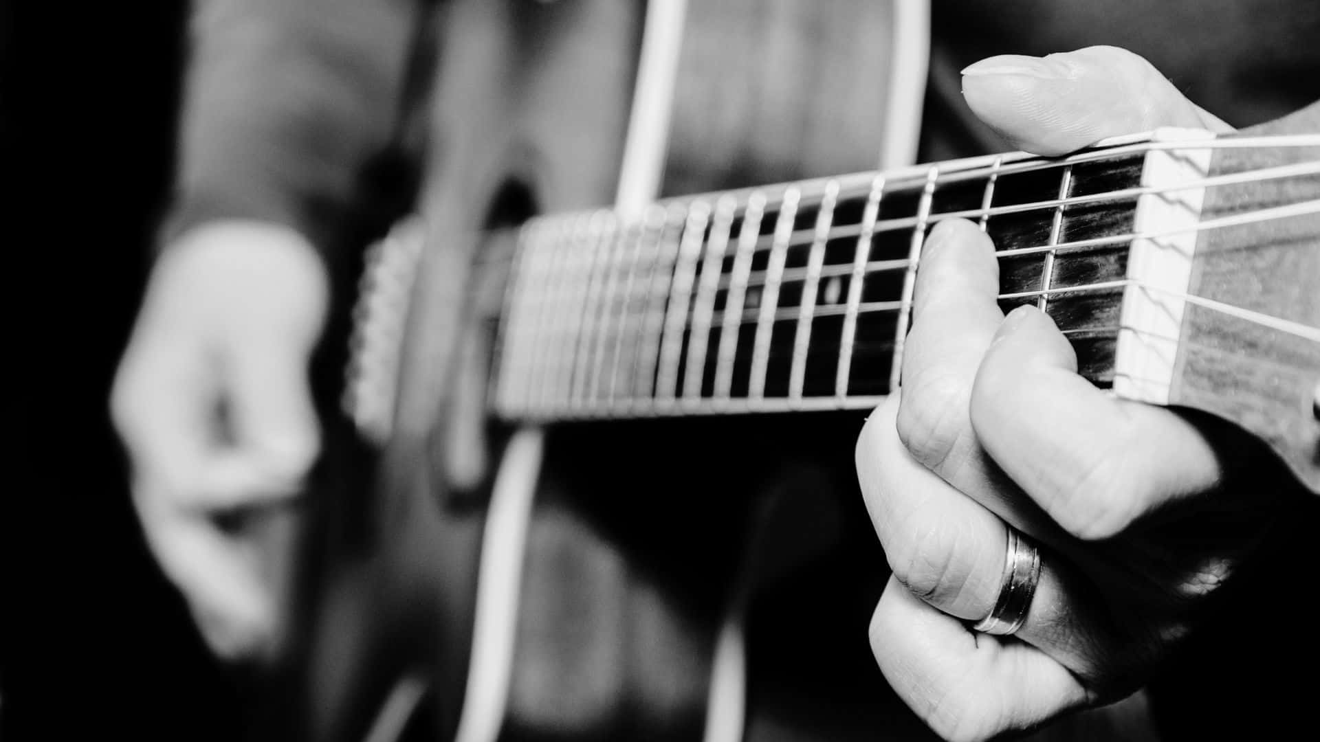 Black And White Guitar 桌布 壁紙 — 一隻戴著戒指的左手熟練地彈奏木吉他的黑白特寫。