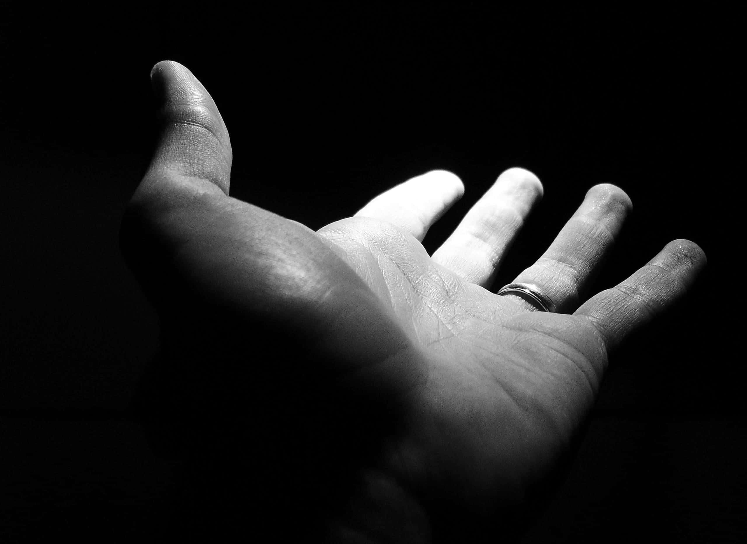 Dark Hand 桌布 壁紙 — 一隻戴著戒指的無名指張開手的黑白特寫，在黑暗背景下戲劇性地打光。