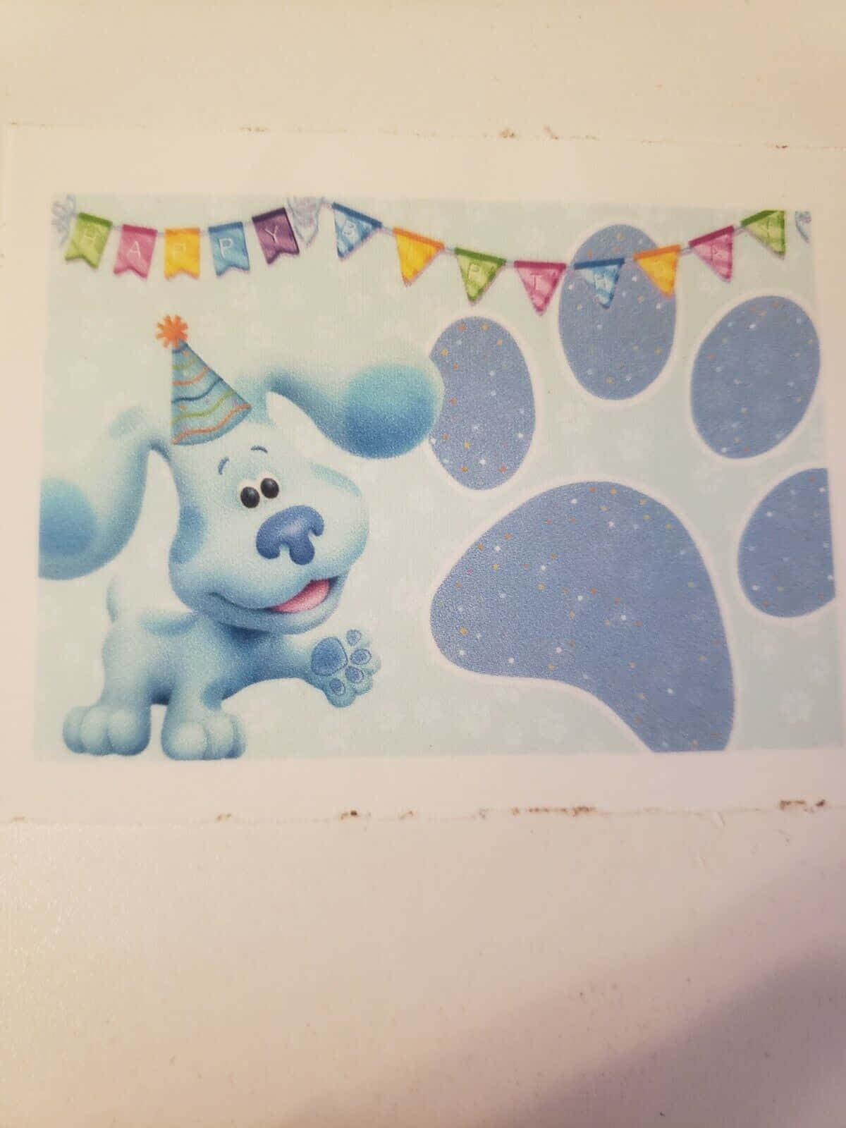 blue's clues 桌布 壁紙 — 一隻戴著派對帽的開心藍色卡通狗站在彩色「Happy Birthday」橫幅下的大藍色腳印旁邊。