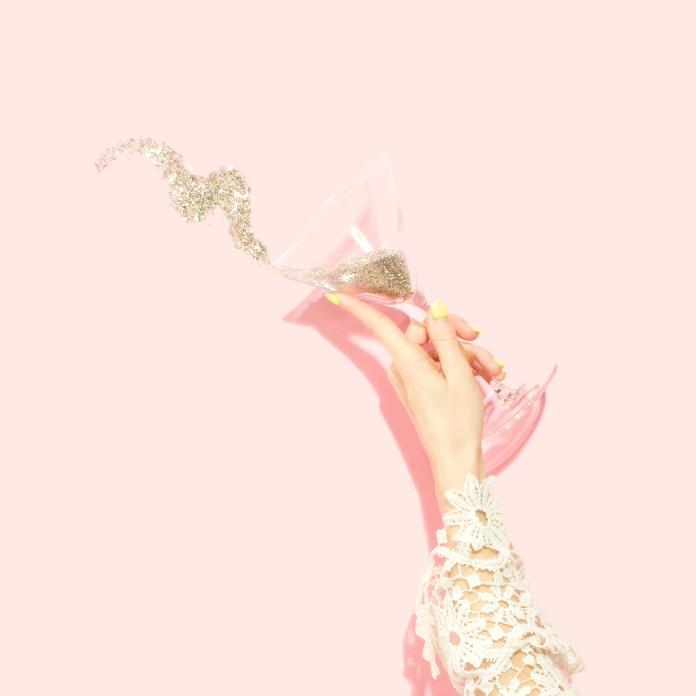 桌布 壁紙 — 一隻戴著蕾絲袖的手拿著一個馬丁尼杯，將亮粉傾斜在柔和的粉紅色背景上。