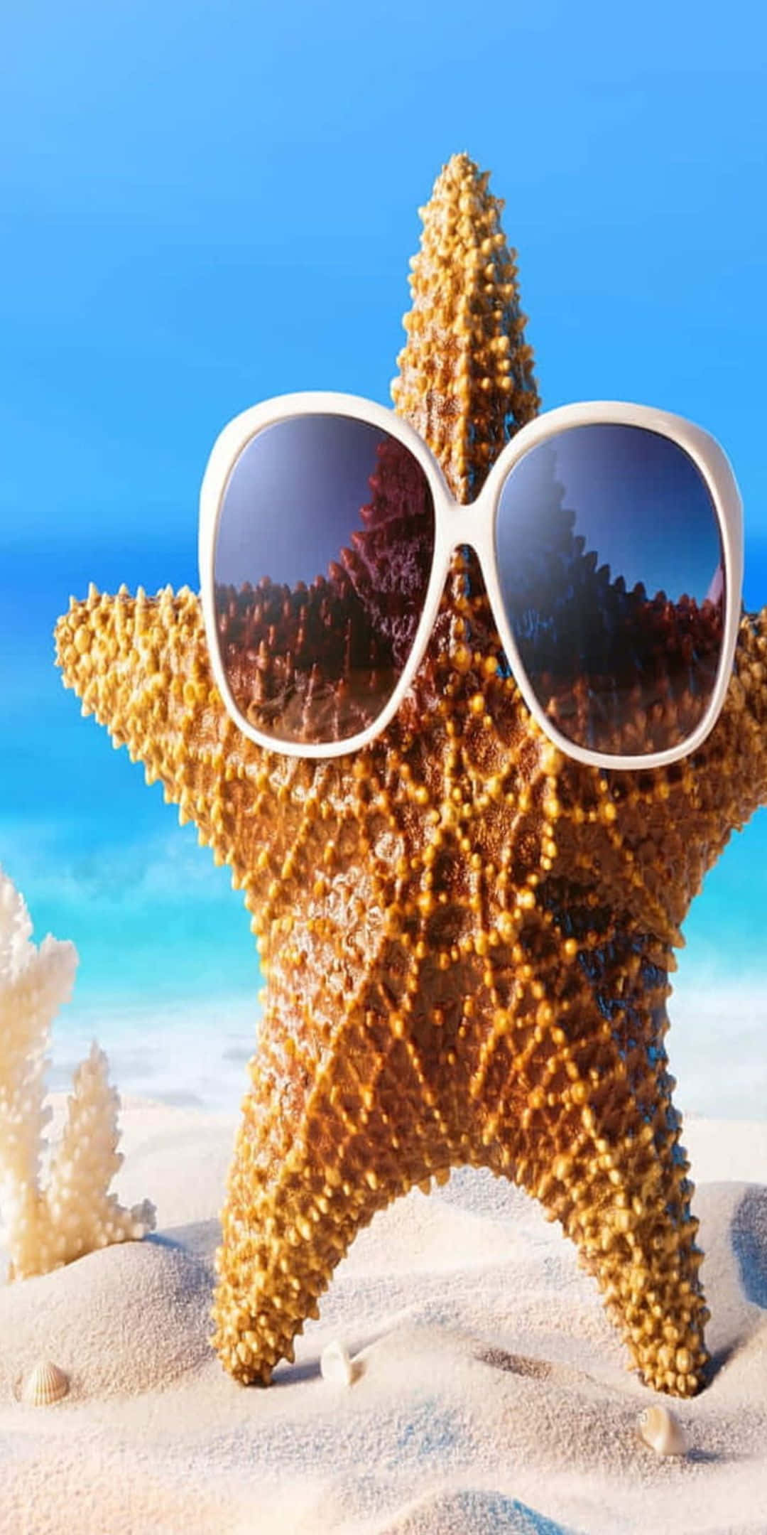 Pixel 3 Summer 桌布 壁紙 — 一隻戴著超大白色太陽眼鏡的開心海星站在沙灘上，背景有珊瑚和碧綠色的海洋。