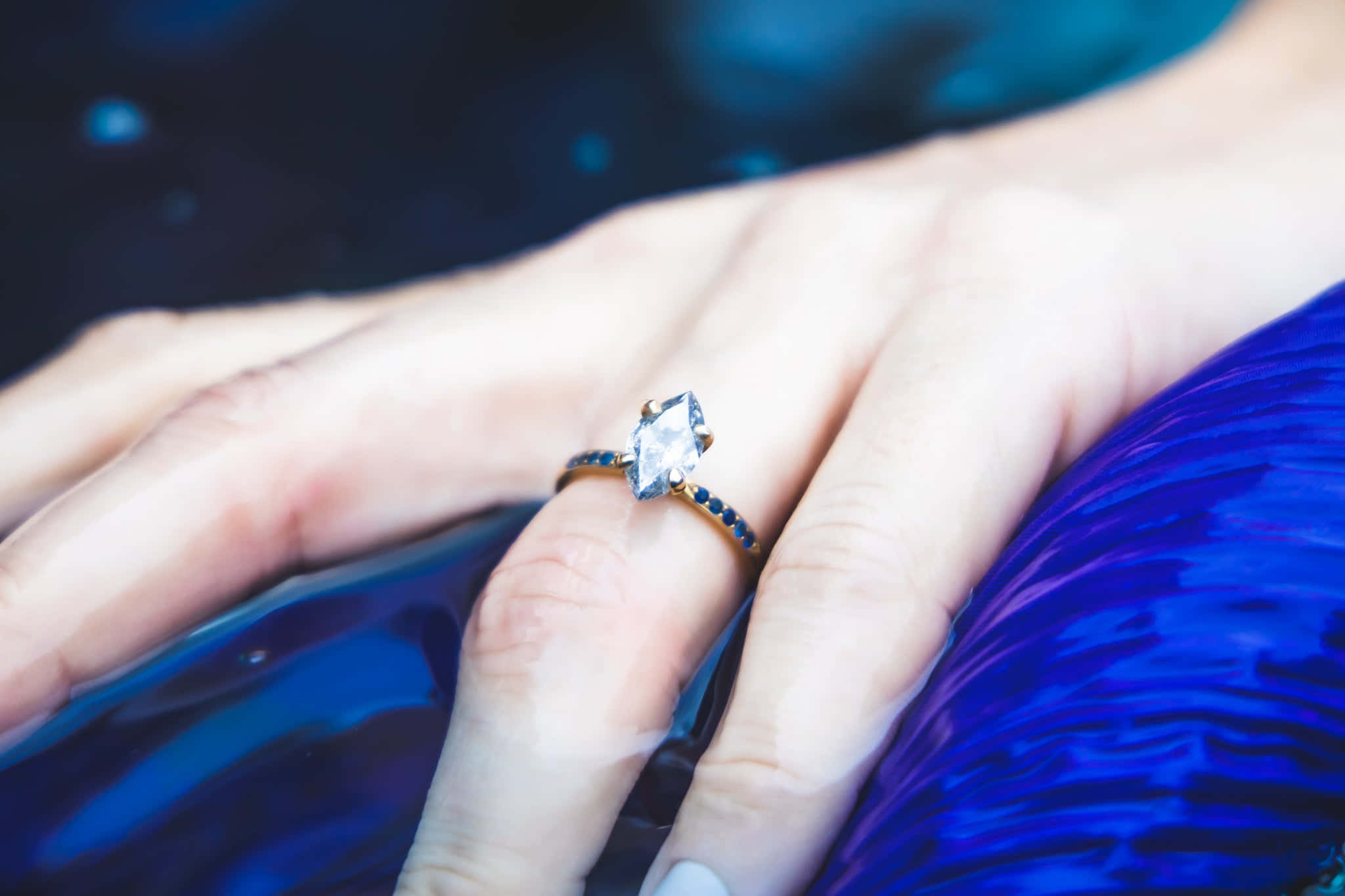 Marriage 桌布 壁紙 — 一隻戴著鑽石戒指的手輕輕放在有紋理的藍色布料上，背景是深色模糊的。