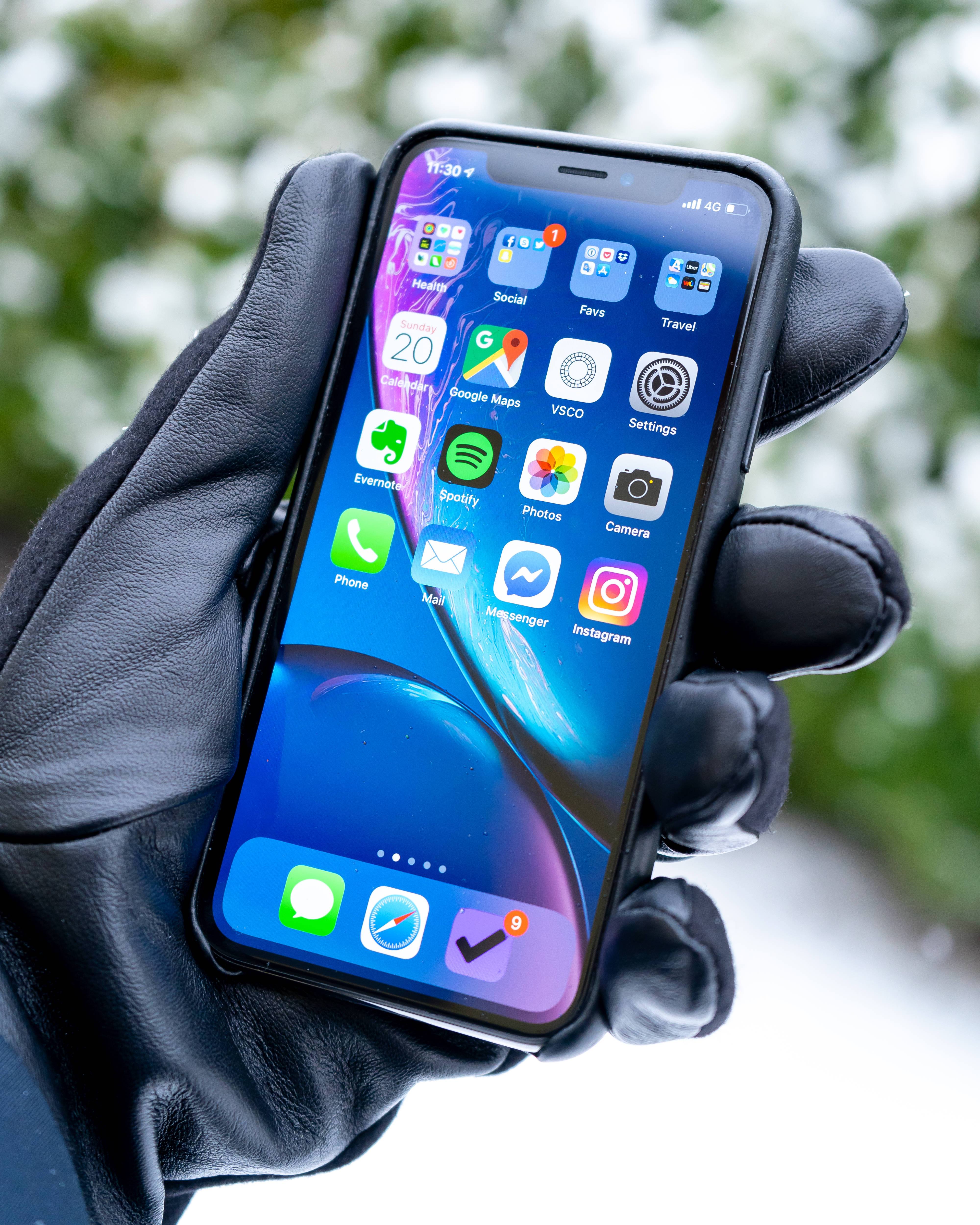 iPhone XS 桌布 壁紙 — 一隻戴著黑色手套的手拿著一支智慧型手機，在雪地戶外背景下顯示充滿活力的應用程式網格。