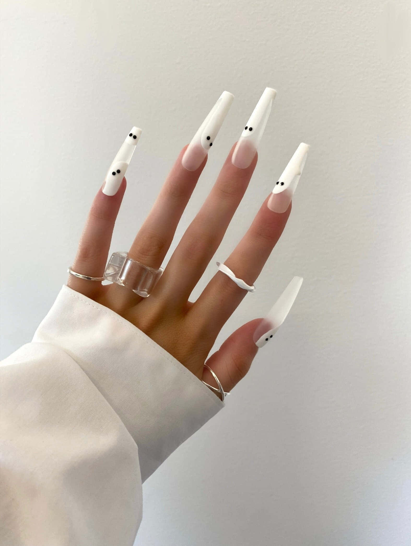 Halloween Nail Art 桌布 壁紙 — 一隻手，帶有長白色棺材形指甲，上面有細小的鬼臉和極簡銀戒指，背景是純白色。