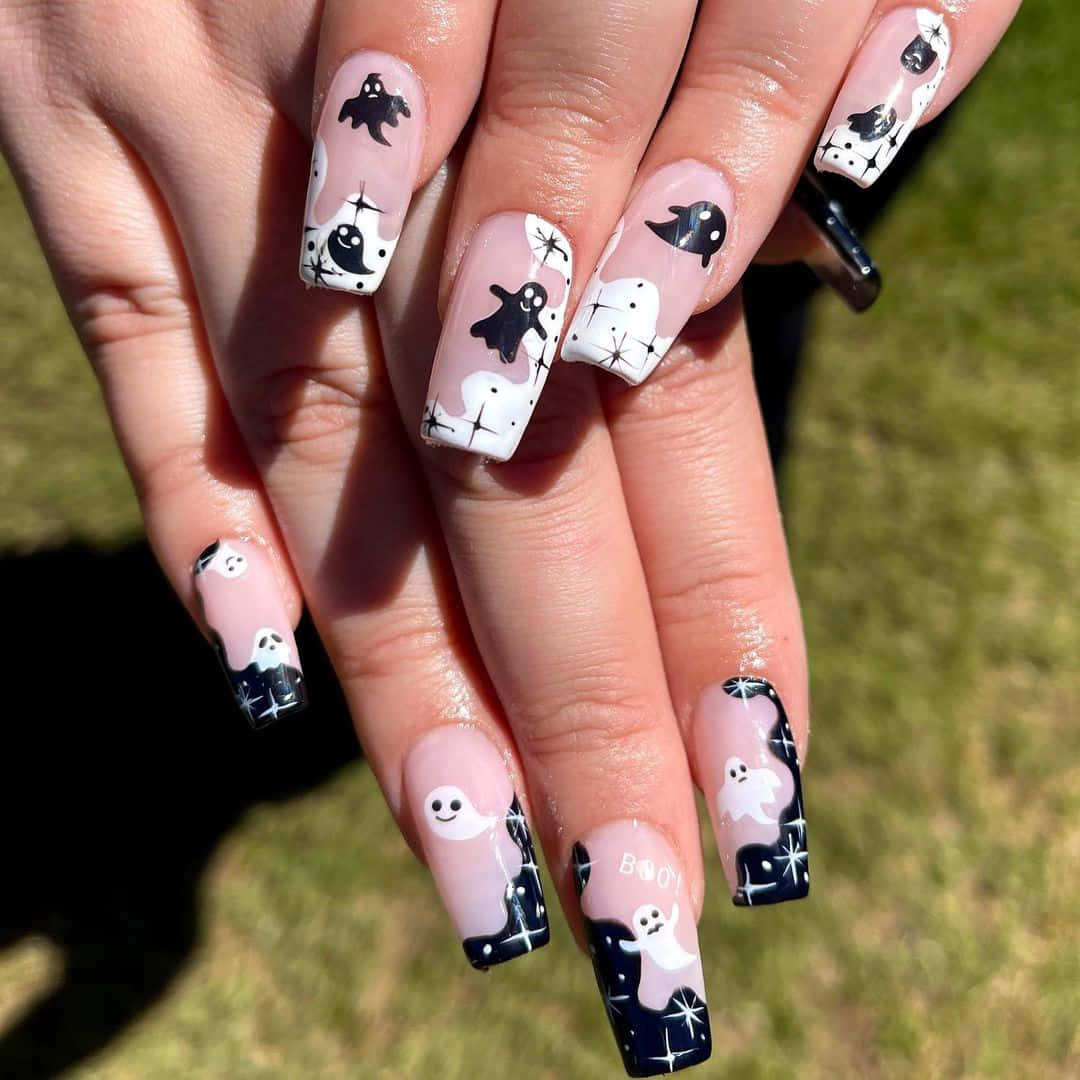 Halloween Nail Art 桌布 壁紙 — 一隻手，指甲呈棺材形狀，帶有可愛的黑白鬼魂設計，背景是陽光明媚的草地。