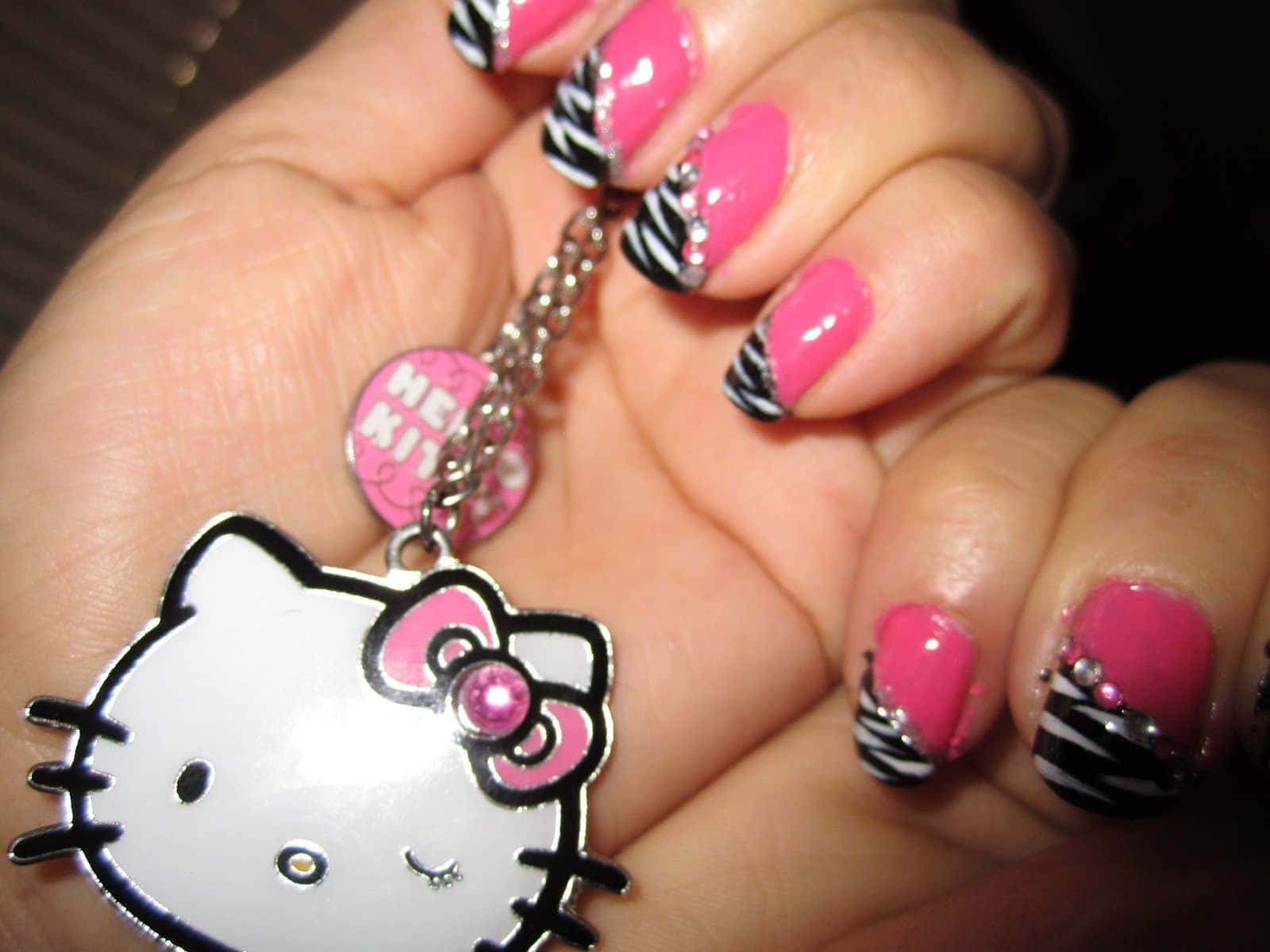 Cute Nails 桌布 壁紙 — 一隻手上有亮粉紅色和黑色斑馬紋指甲，拿著一個帶有閃亮粉紅色蝴蝶結的Hello Kitty鑰匙圈。