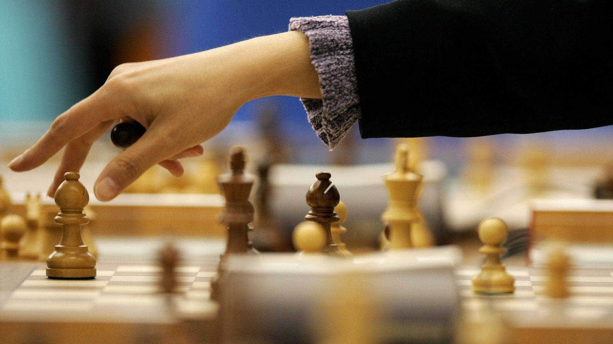 西洋棋 桌布 壁紙 — 一隻手伸向木製棋盤上移動西洋棋兵的特寫，背景有模糊的棋子。