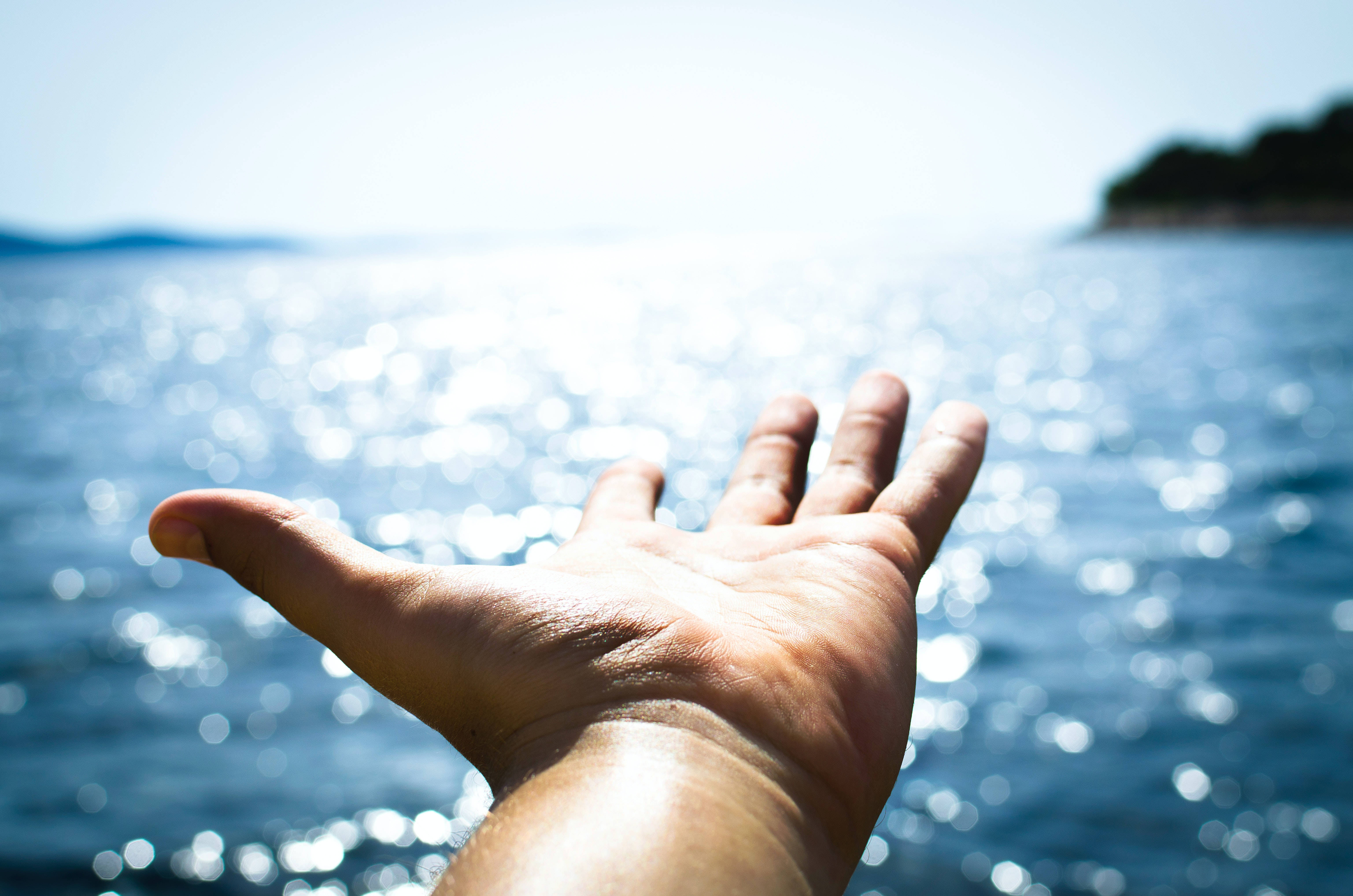 hands 桌布 壁紙 — 一隻手伸向陽光普照的海洋，背景是閃閃發光的水面。