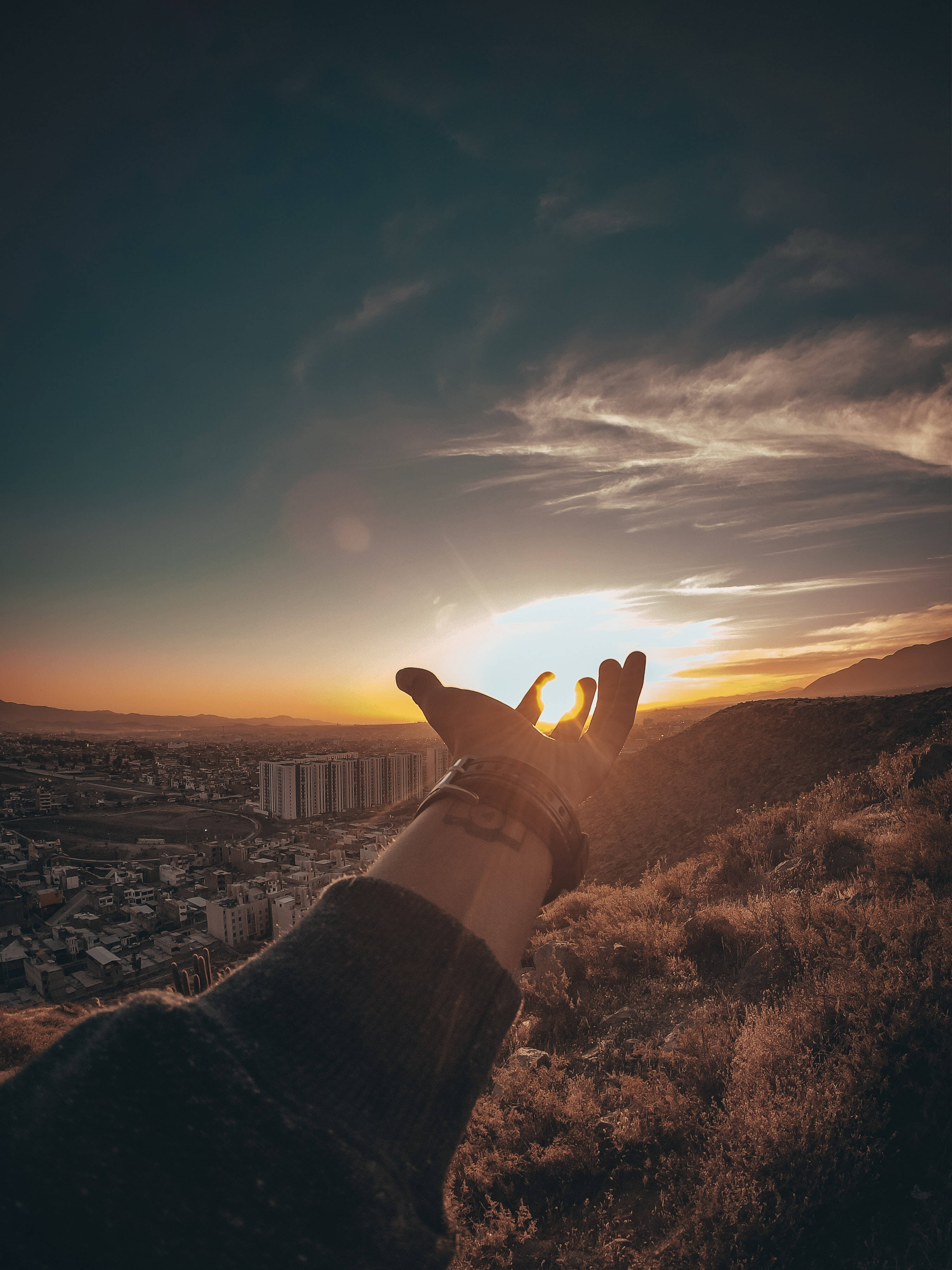 太陽 桌布 壁紙 — 一隻手伸向黃金時段廣闊城市景觀上方的夕陽。