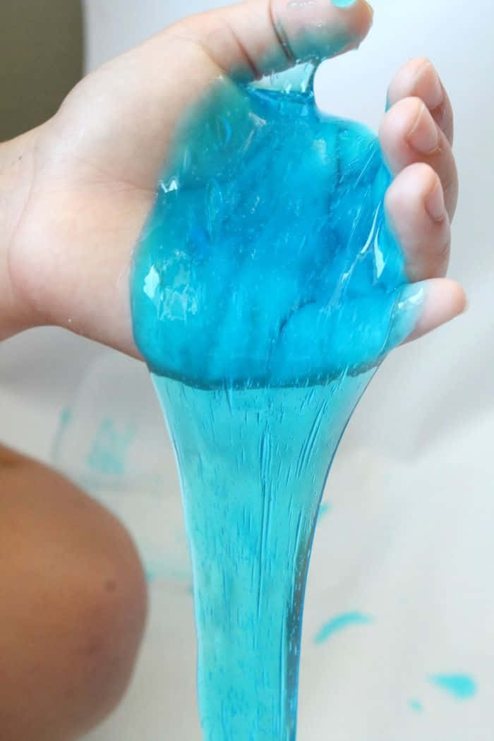 slime 桌布 壁紙 — 一隻手伸展出鮮豔的藍色史萊姆，緩慢地滴落成光澤黏稠的流體。
