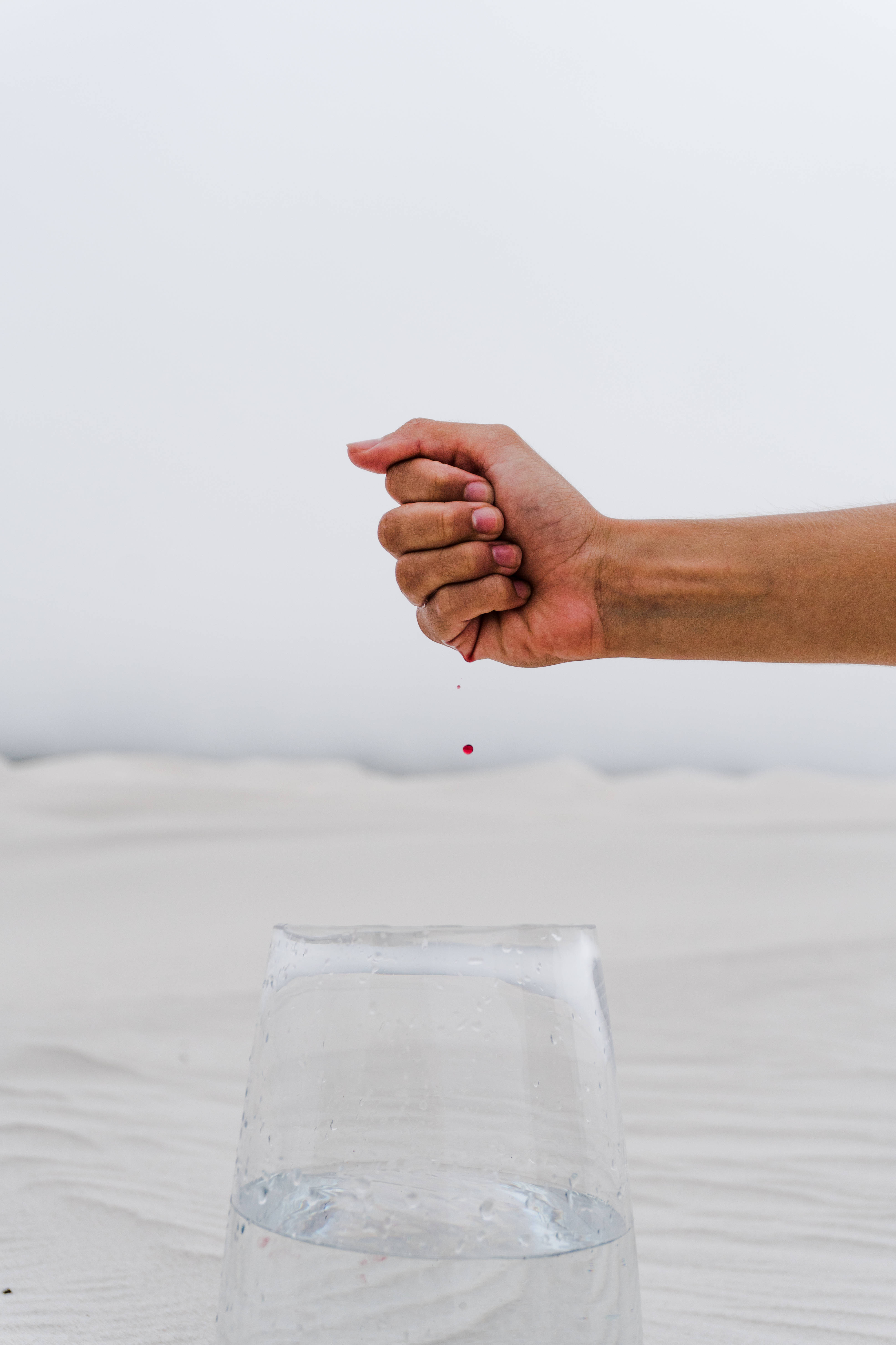 Blood 桌布 壁紙 — 一隻手在一杯水上方握緊，一滴紅色的水滴落在下面的沙上。