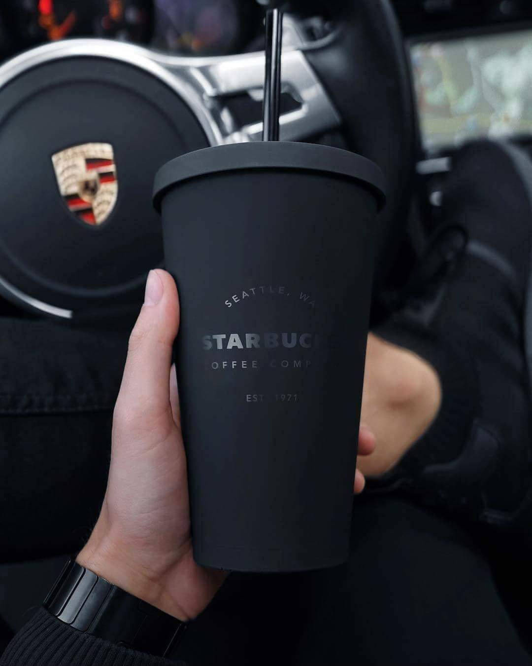 在保時捷車內手持黑色星巴克咖啡杯。