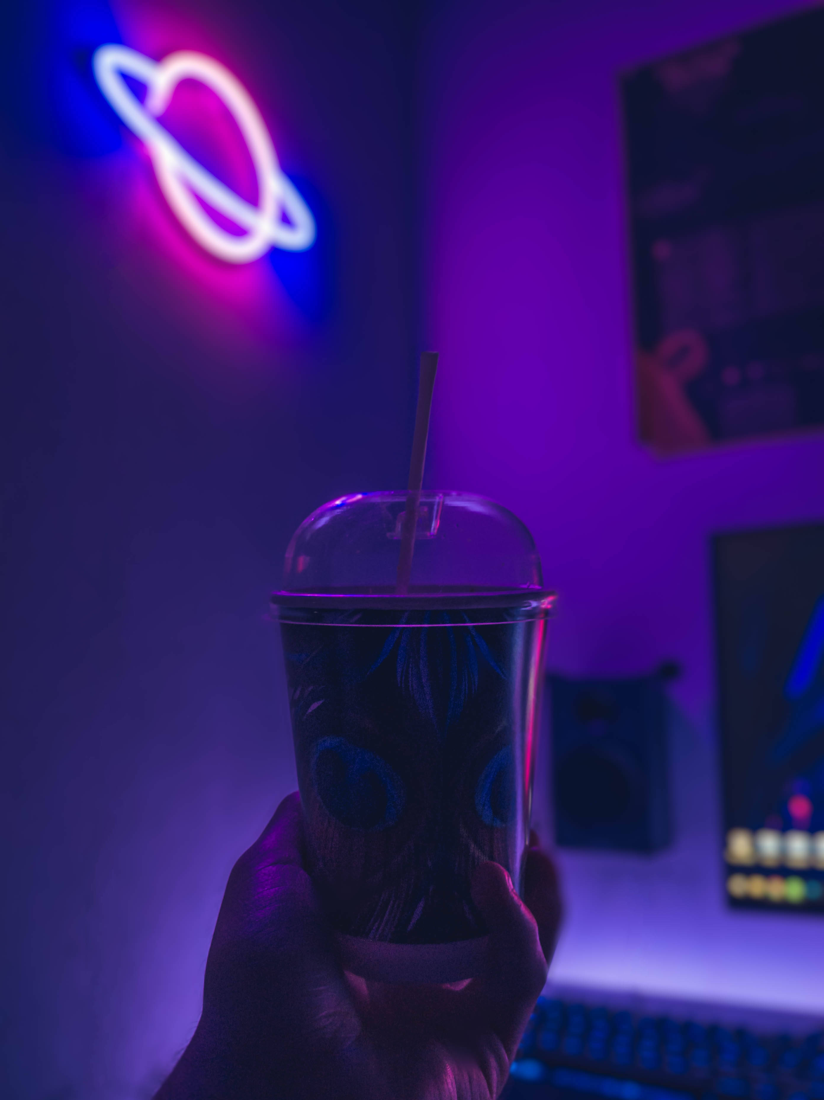 霓虹紫美學 桌布 壁紙 — 一隻手在充滿未來感的遊戲室中，在鮮豔的紫色和粉紅色霓虹燈光下拿著發光的飲料。