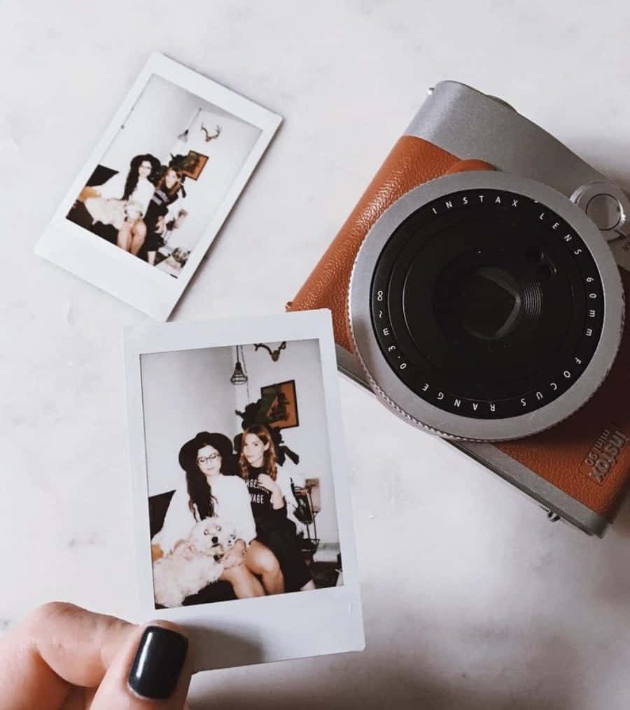 拍立得 桌布 壁紙 — 一隻手在大理石表面上，在一台復古 Instax 相機旁邊，拿著一張有兩個女人和一隻狗的拍立得照片。