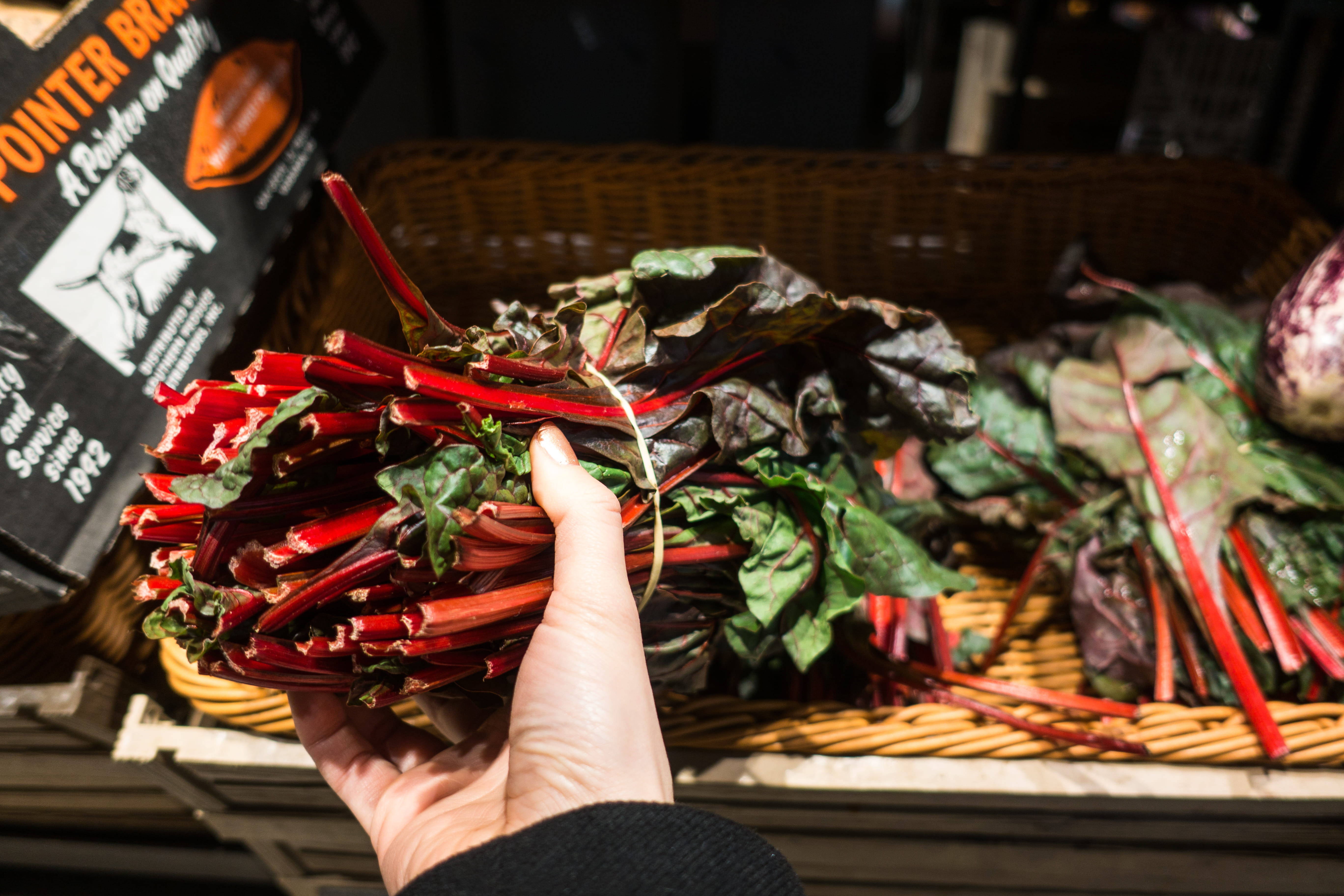 Rhubarb 桌布 壁紙 — 一隻手在市場攤位上拿著一束鮮豔的紅梗瑞士甜菜，葉子深綠色。