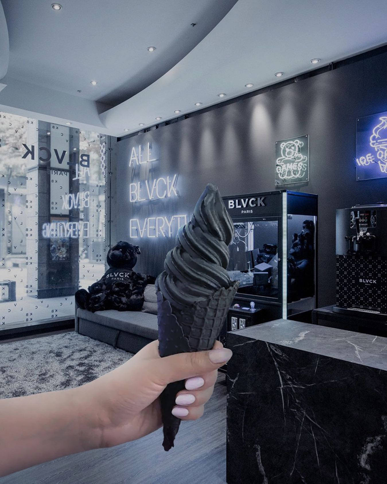 Ice Cream 桌布 壁紙 — 一隻手在時尚現代黑色室內環境中拿著一個黑色漩渦冰淇淋甜筒，周圍有霓虹燈牌和一個毛絨黑色泰迪熊。