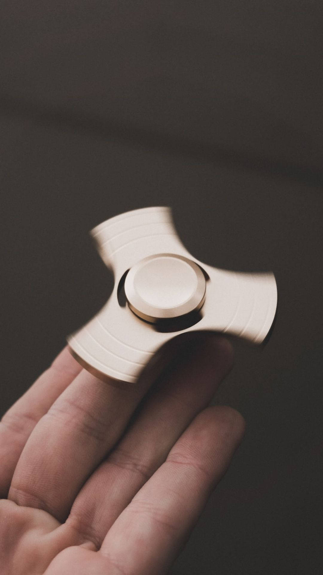 toys 桌布 壁紙 — 一隻手在暗色柔和背景前握著一個旋轉的銀色指尖陀螺。