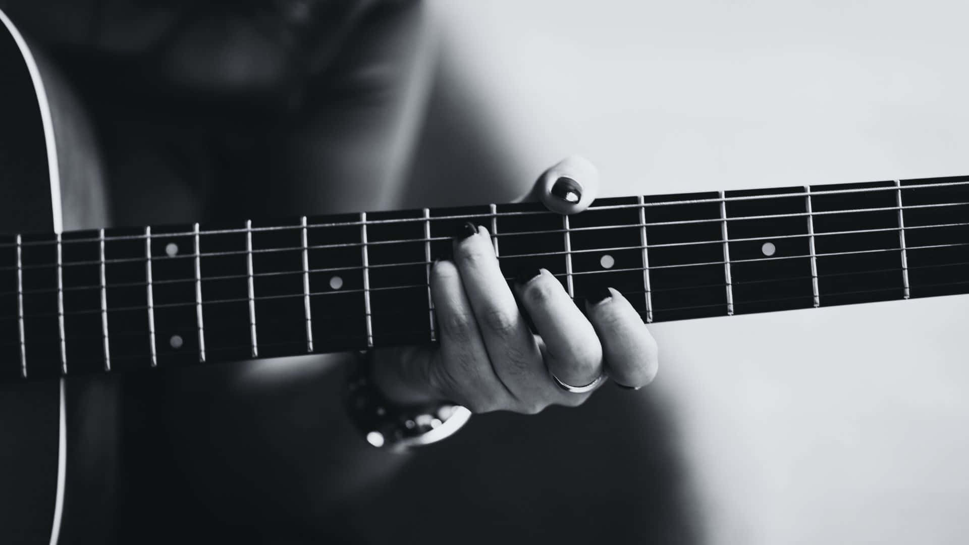 Black And White Guitar 桌布 壁紙 — 一隻手在木吉他指板上按弦的黑白特寫，戒指和手錶清晰可見。