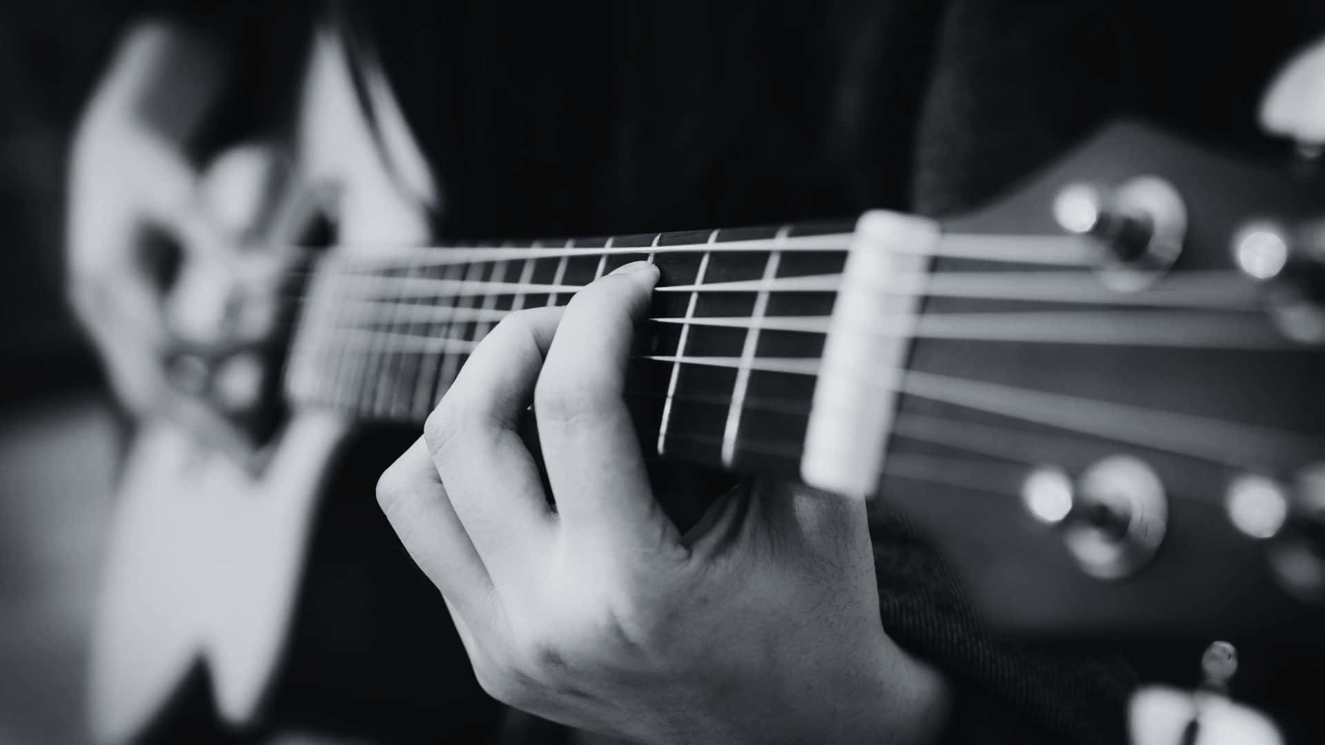 Black And White Guitar 桌布 壁紙 — 一隻手在木吉他琴頸上按弦的黑白特寫，背景模糊。