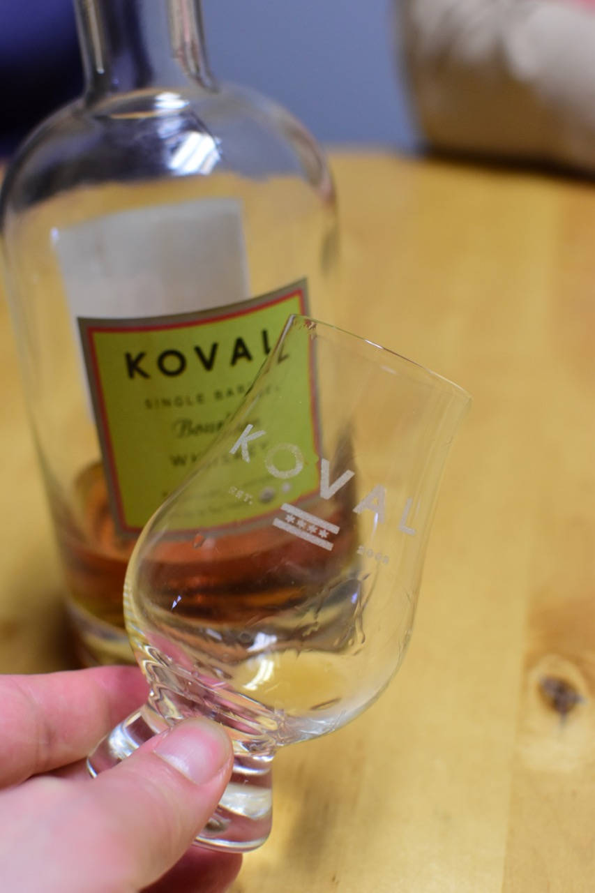alcohol 桌布 壁紙 — 一隻手在木桌上的酒瓶前面拿著一個Koval威士忌品酒杯。