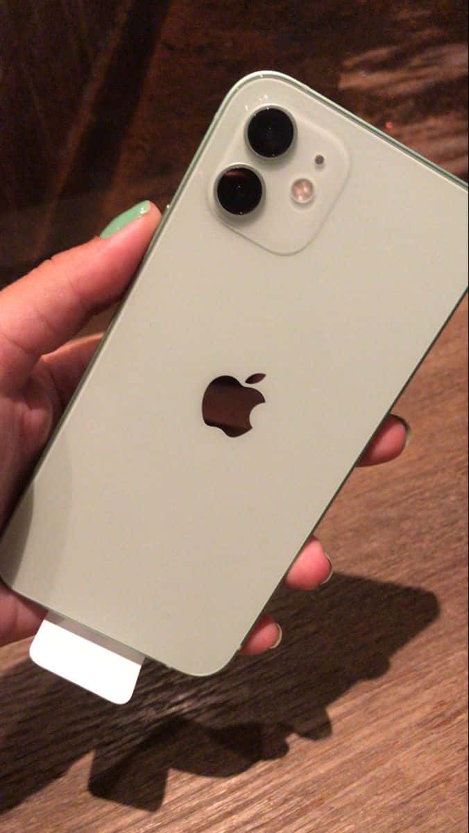 iPhone 12 桌布 壁紙 — 一隻手在木質表面上拿著一部淺綠色的iPhone 12 mini，配備雙鏡頭。