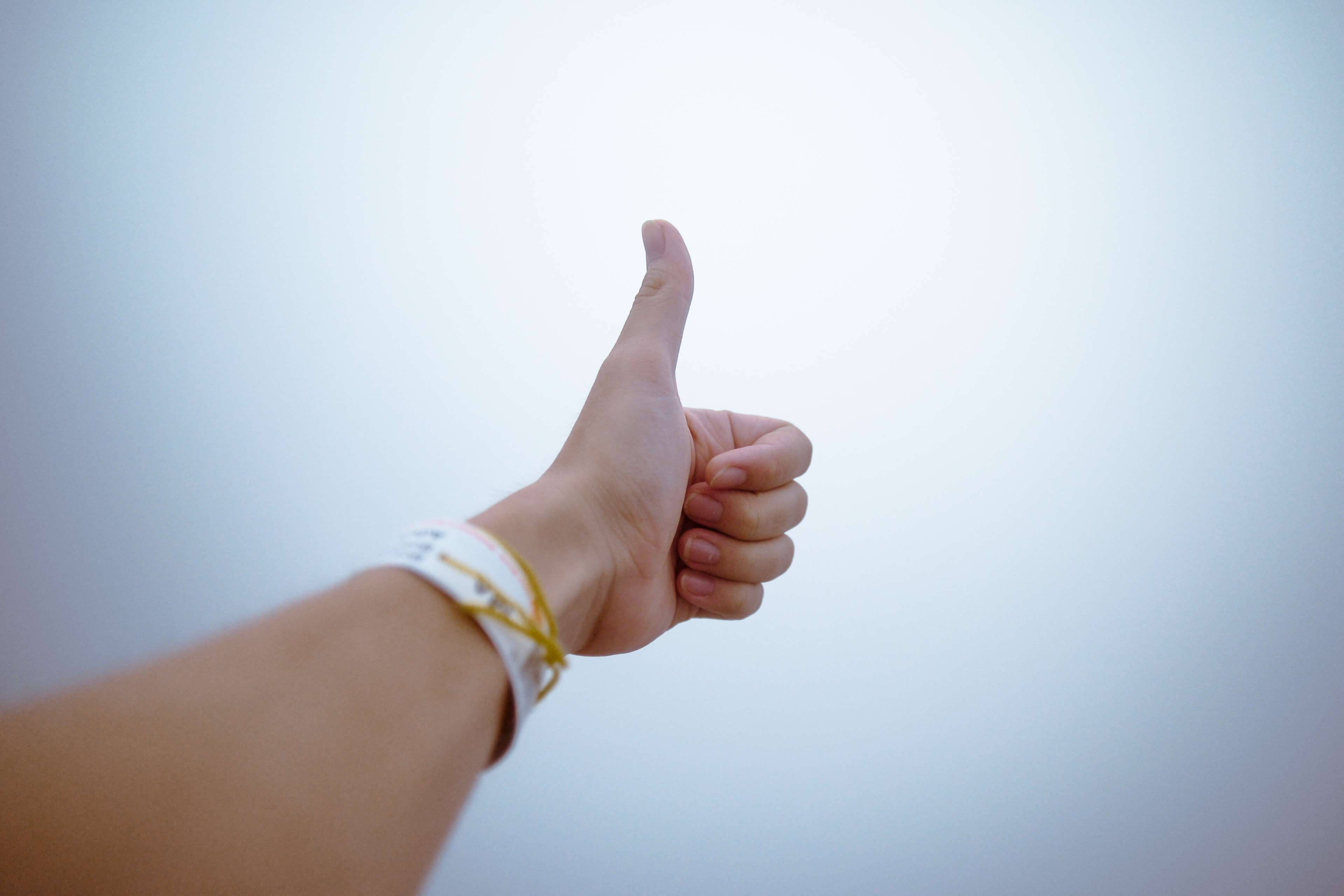 Thumbs Up 桌布 壁紙 — 一隻手在柔和漸層的天空背景下做出豎起大拇指的手勢，手腕帶清晰可見。