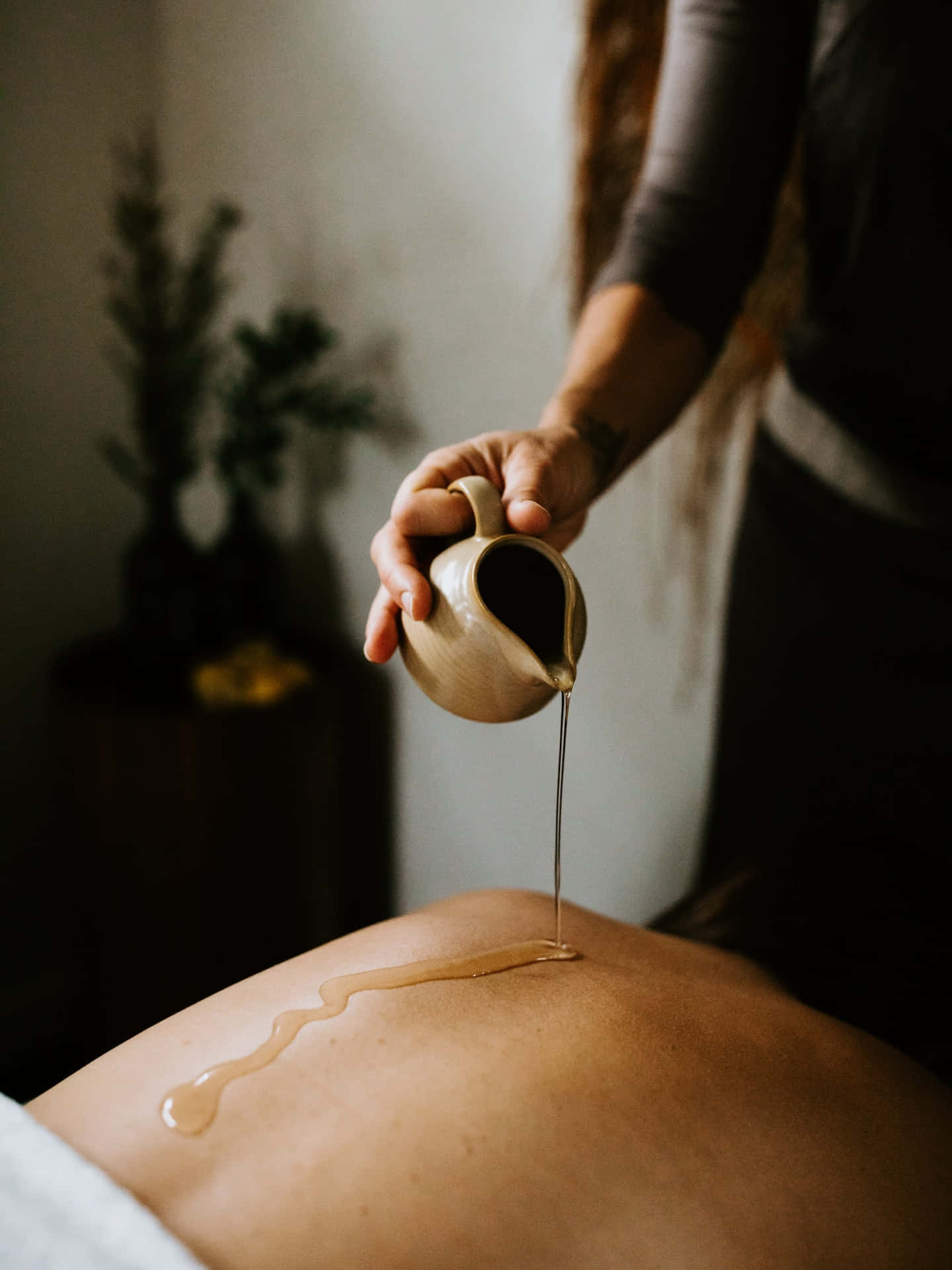 Massage 桌布 壁紙 — 一隻手在柔和燈光的溫泉環境中，將溫暖的金色油緩慢地倒在裸露的背上。