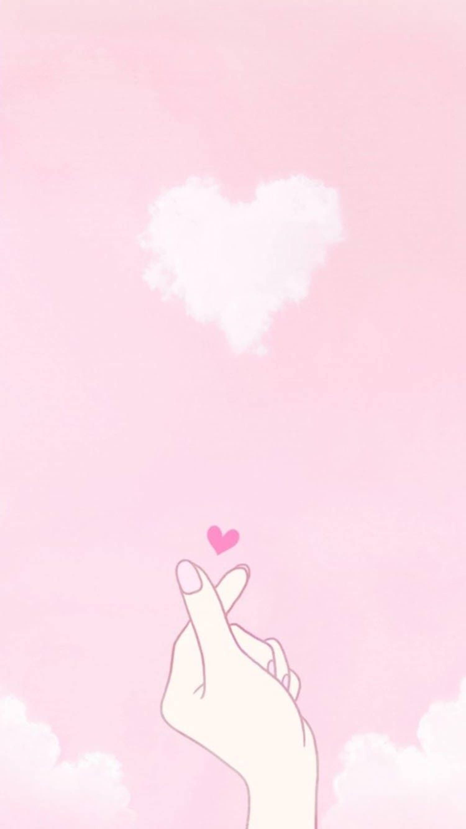 Pastel Pink Heart 桌布 壁紙 — 一隻手在柔和的粉紅色天空下，在一個蓬鬆的白色心形雲朵下方做出心形手勢。
