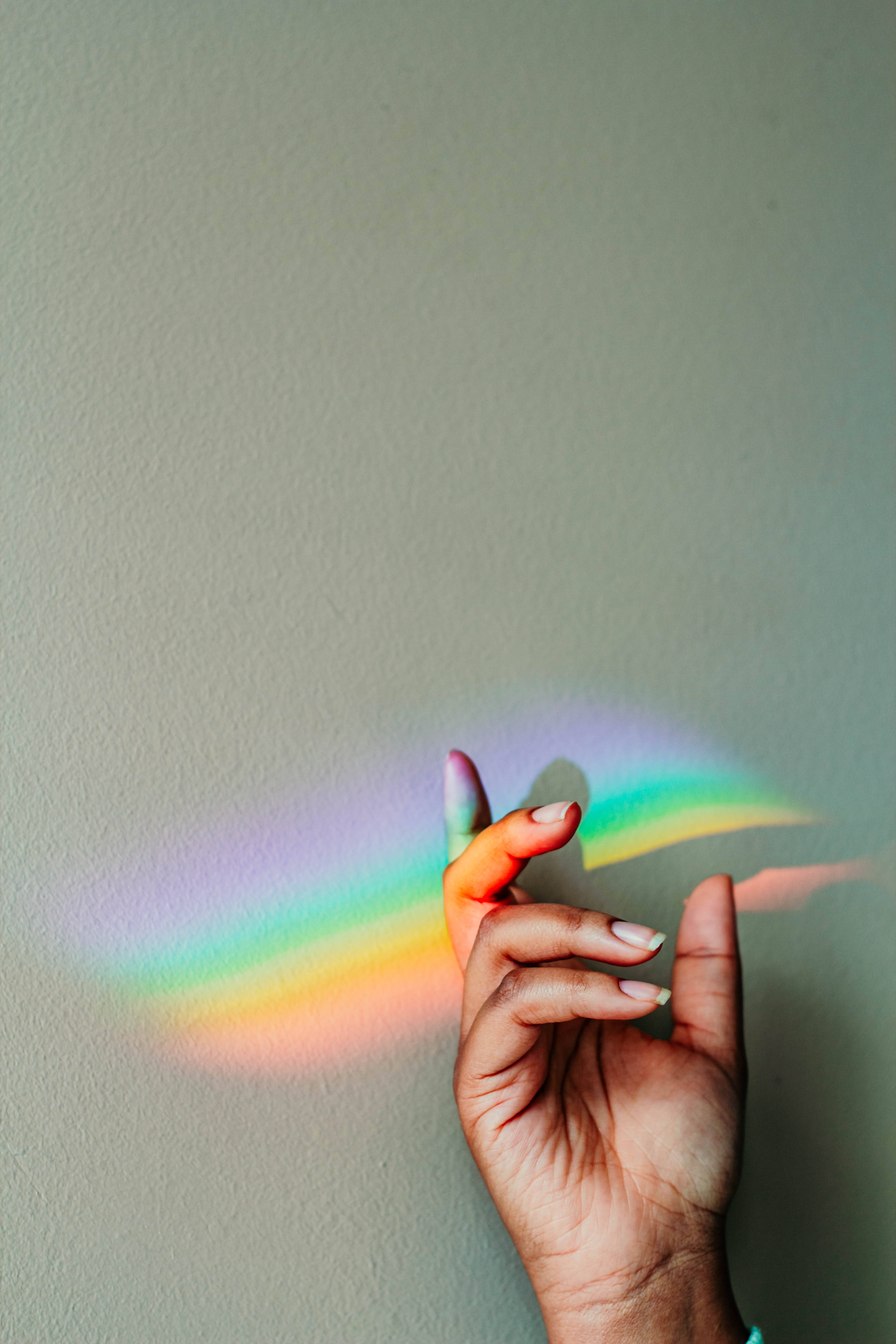Prism 桌布 壁紙 — 一隻手在柔和自然光下，於素牆上投射出鮮豔的彩虹稜鏡陰影。