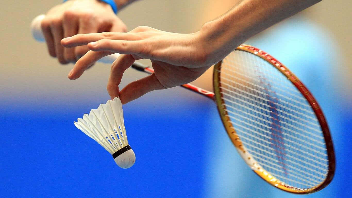 1366x768 Badminton 桌布 壁紙 — 一隻手在模糊的藍色背景下，優雅地拿著羽毛球靠近球拍的近距離特寫。
